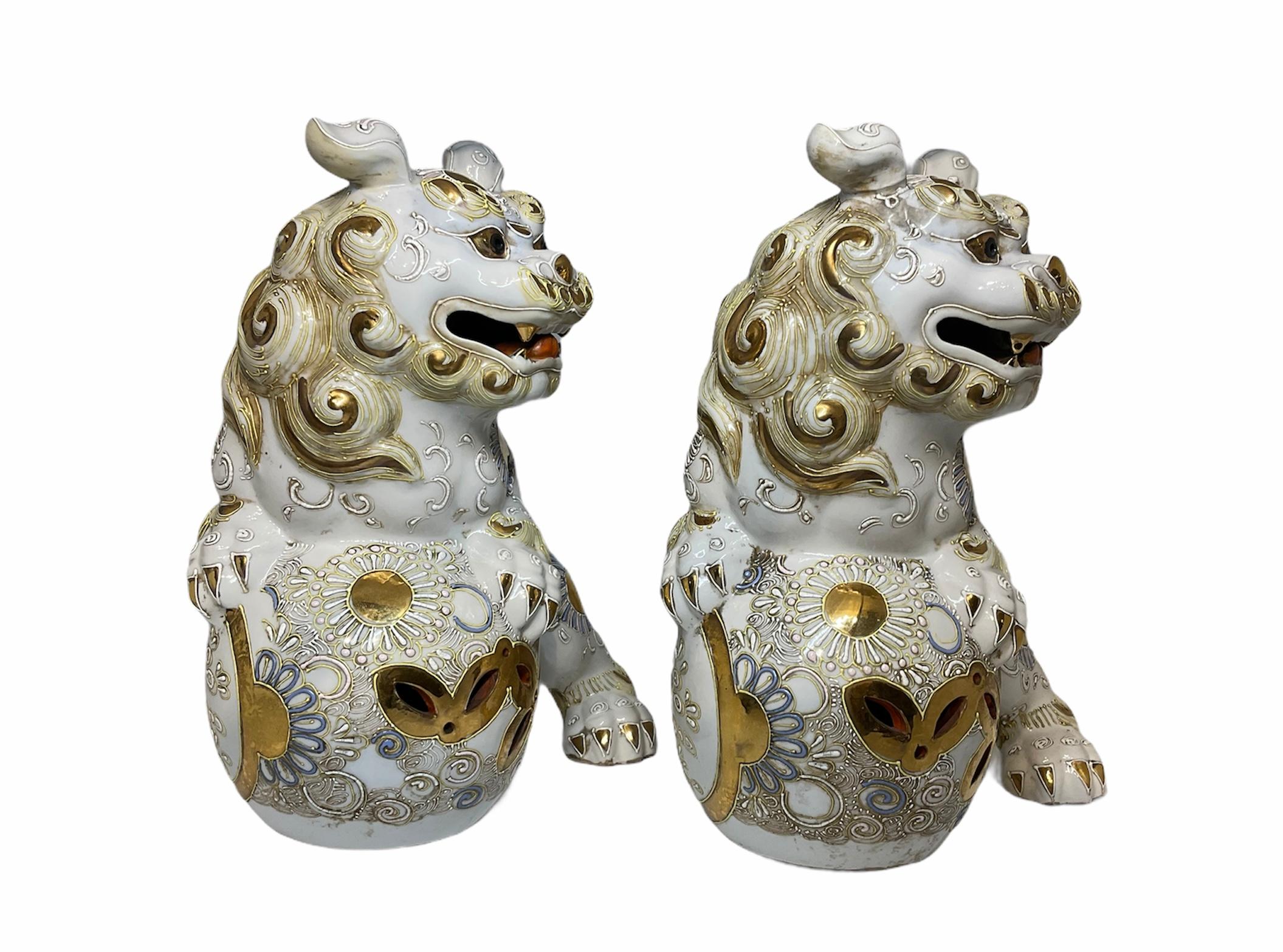 This is a pair of Japanese Satsuma Kutani porcelain Foo Dogs. They are hand painted white and adorned with gilt and silver suns, flowers and scrolls. Both of them are playing with a ball decorated in the same way. Foo dogs or guardian lions