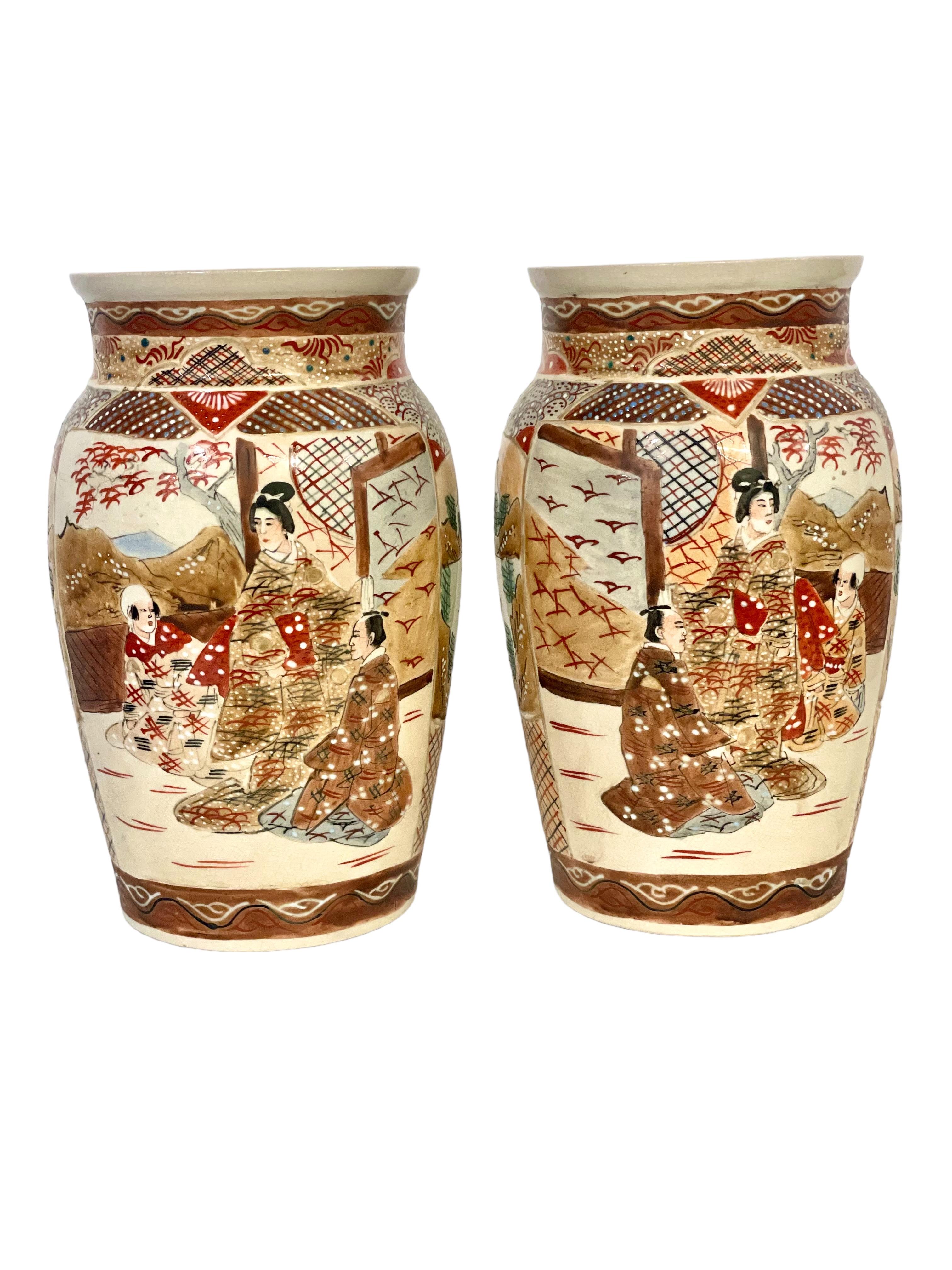 A fine pair of Japanese Satsuma earthenware vases, ornately decorated in typical Satsuma colours with enamels and heavy gilding. The designs on the bodies of these late 19th century or early 20th century shouldered vases feature traditional figural