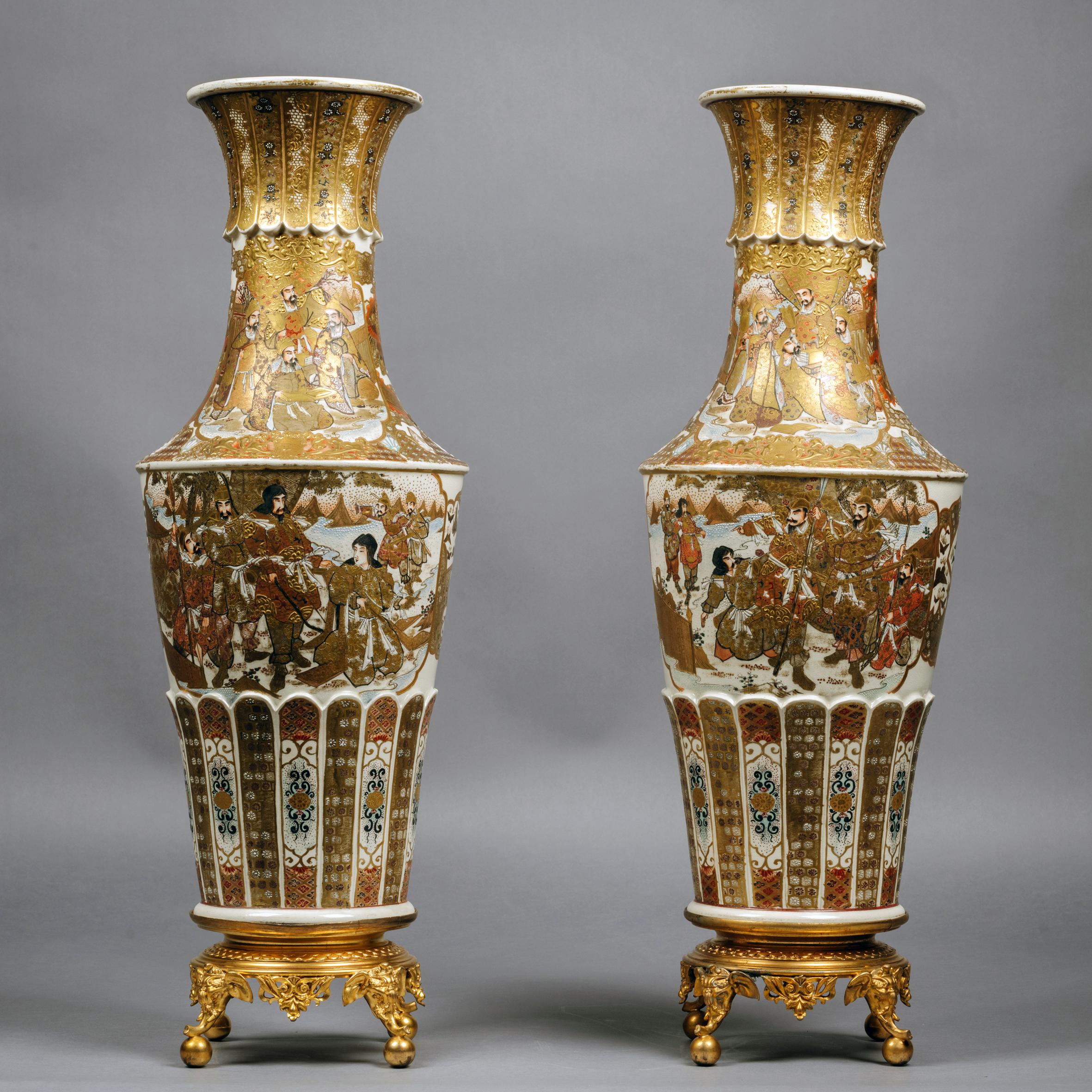 A fine pair of Japanese Satsuma vases raised on gilt-bronze bases.

Each vase with an elongated trumpet shaped neck and tapering cylindrical body, painted and gilt with panels of warriors and officers in a stylised landscape, surrounded by floral