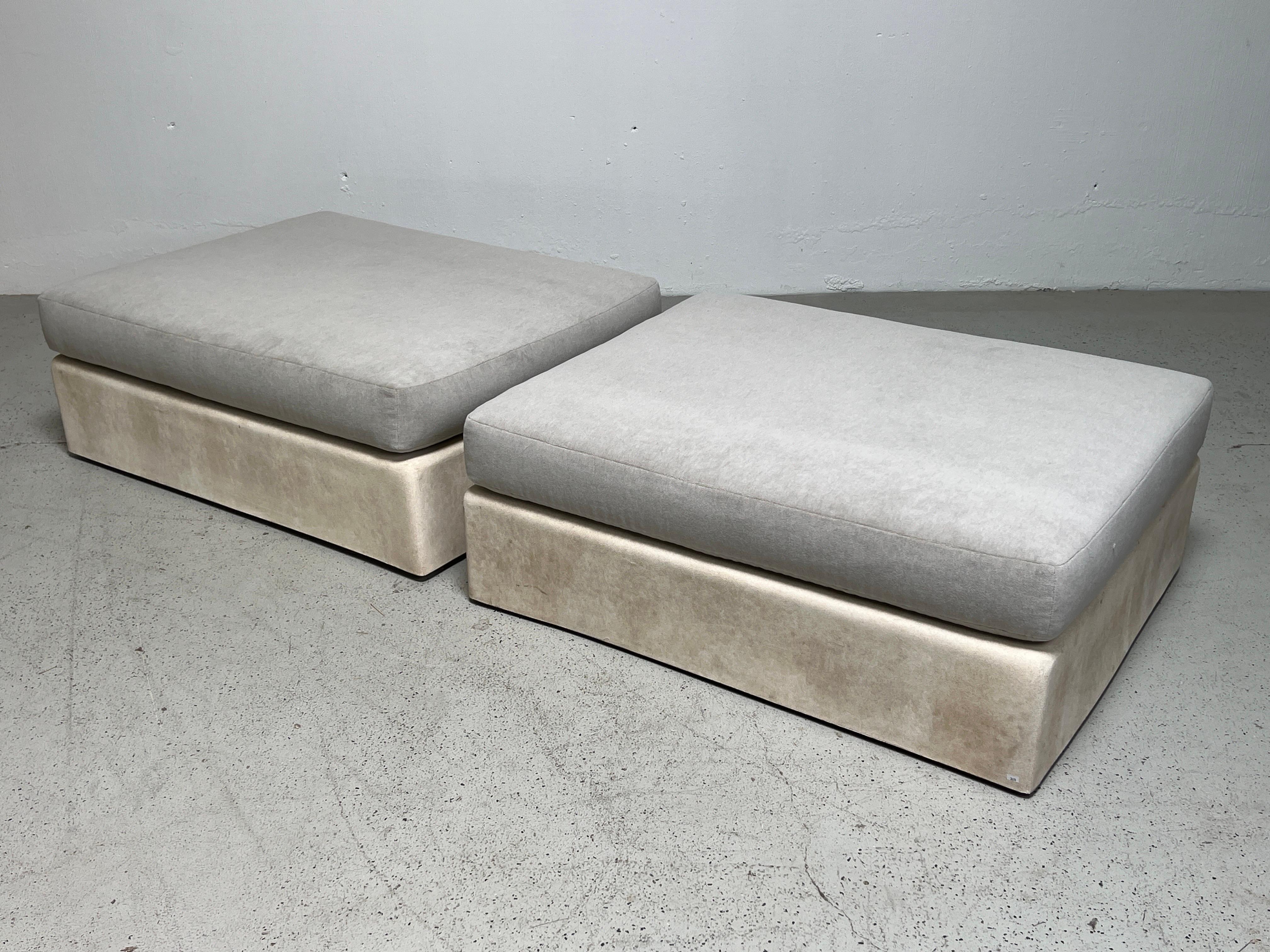 A pair of large scale Jennifer ottomans designed by Michael Taylor. The fiberglass frames are covered in a Spanish plaster finish and sit on hidden casters. Each ottoman weights approximately 100 pounds. These have been reupholstered in Holly Hunt /
