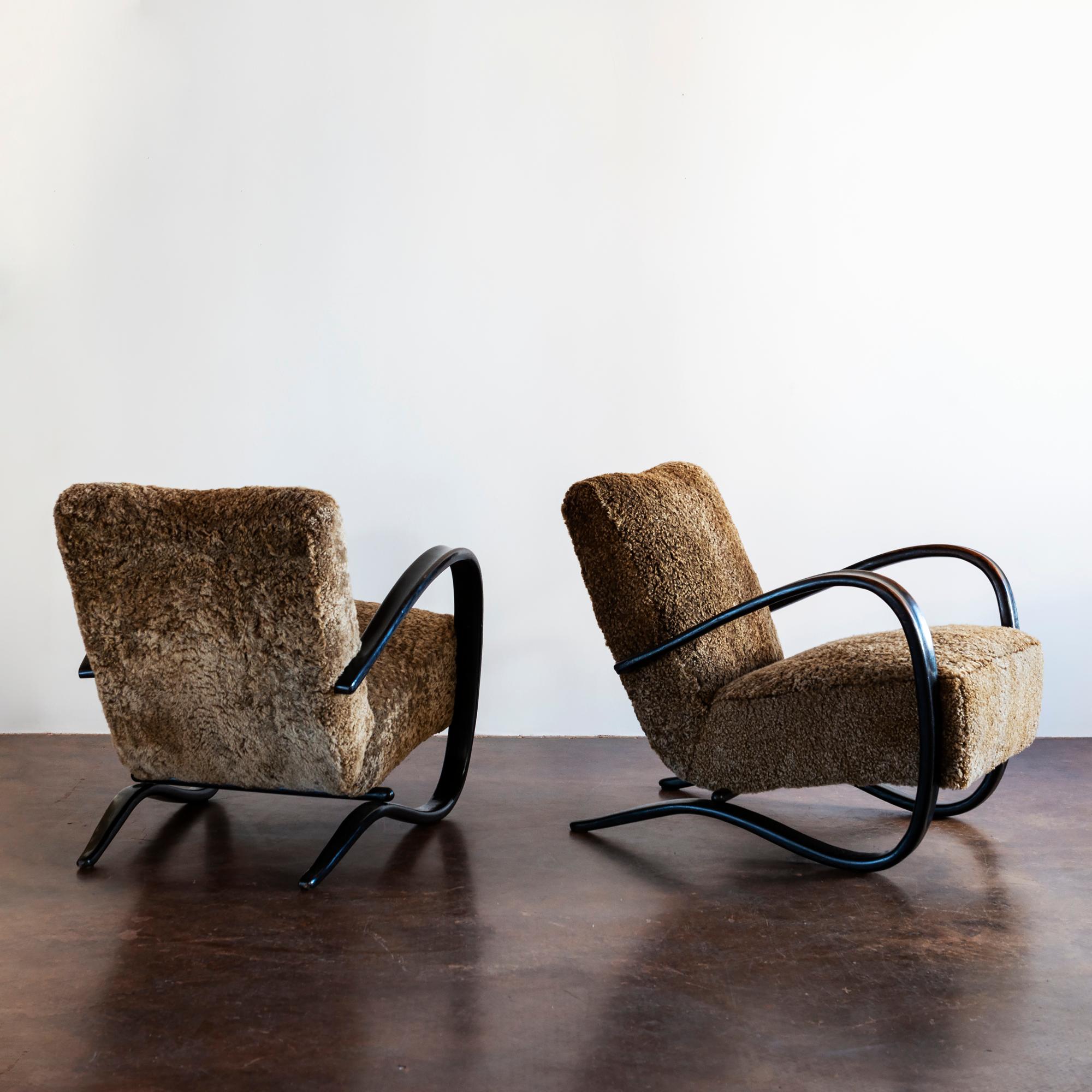Pair of iconic Halabala 269 lounge chairs in patinated beechwood, recently reupholstered in exquisite cafe-colored sheepskin, Czechoslovakia, 1930s.