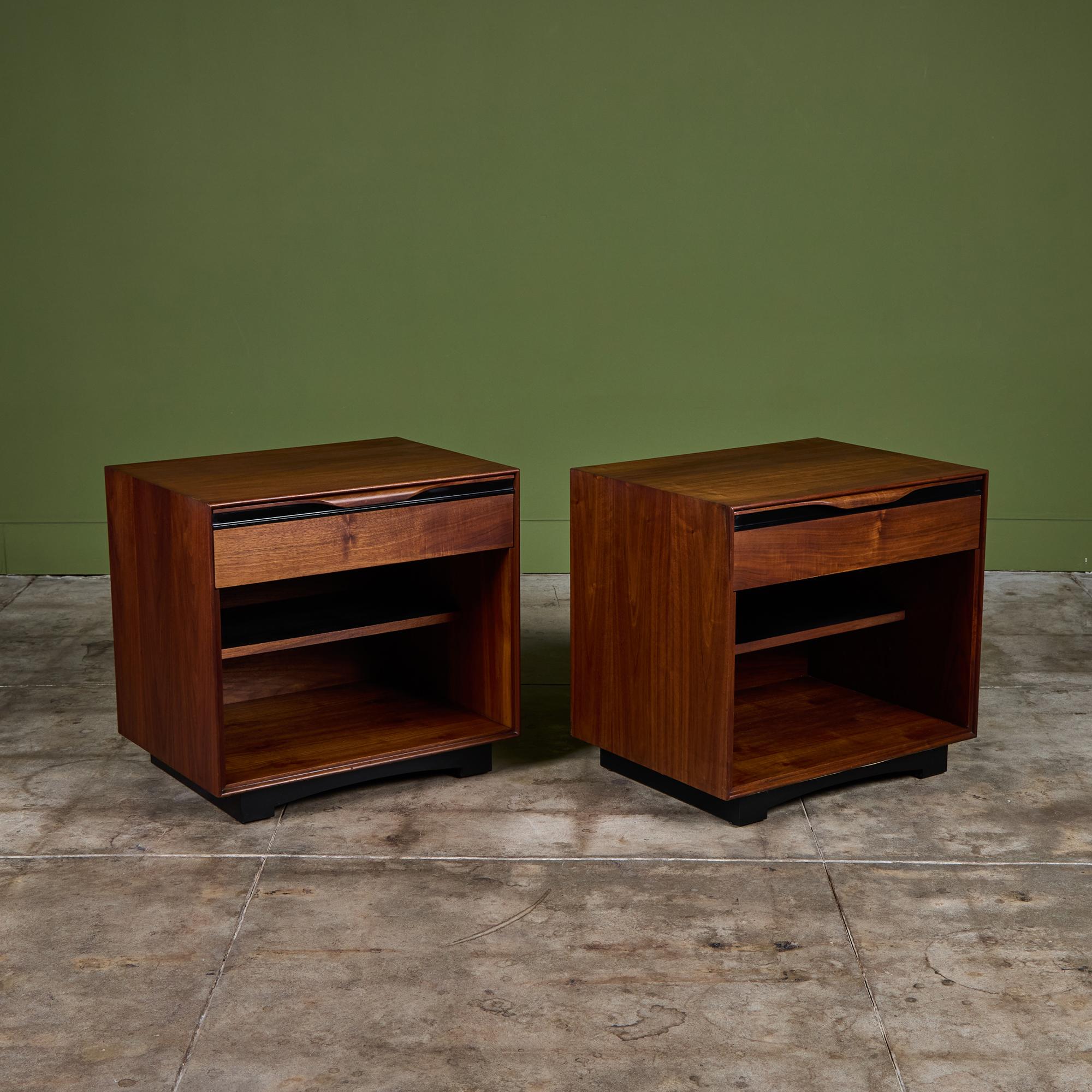 Pair of walnut nightstands by John Kapel for Glenn of California, c.1960s, USA. The nightstands each feature a single drawer with sculpted handles and black linear detailing. Each nightstand has open shelving below the drawer and rests on an