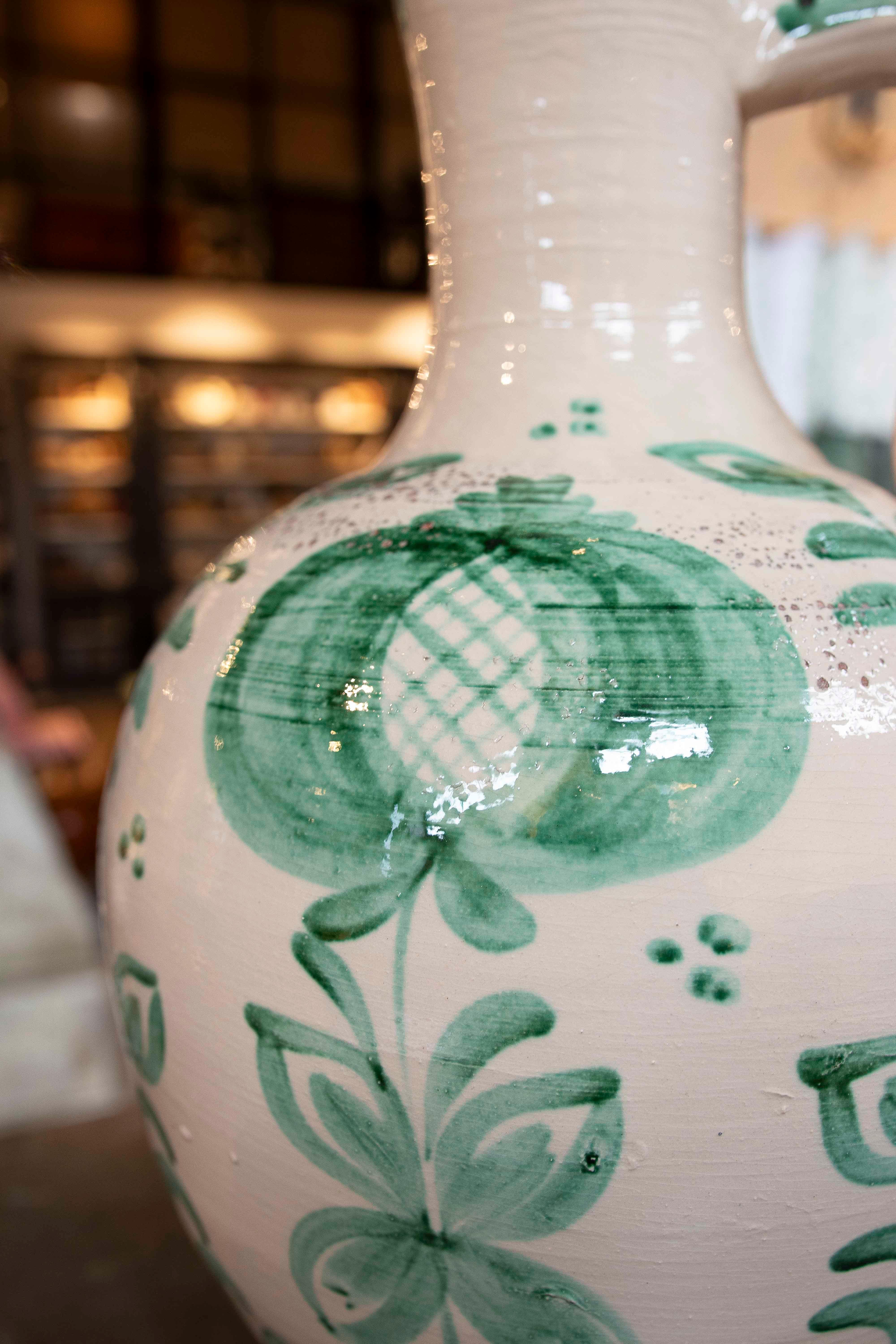 Paire de lampes de table décoratives fabriquées à partir de cruches en céramique traditionnelle, émaillées en blanc avec des motifs de plantes vertes. Leur design incurvé et élégant, avec une poignée latérale et un col étroit, rappelle les poteries