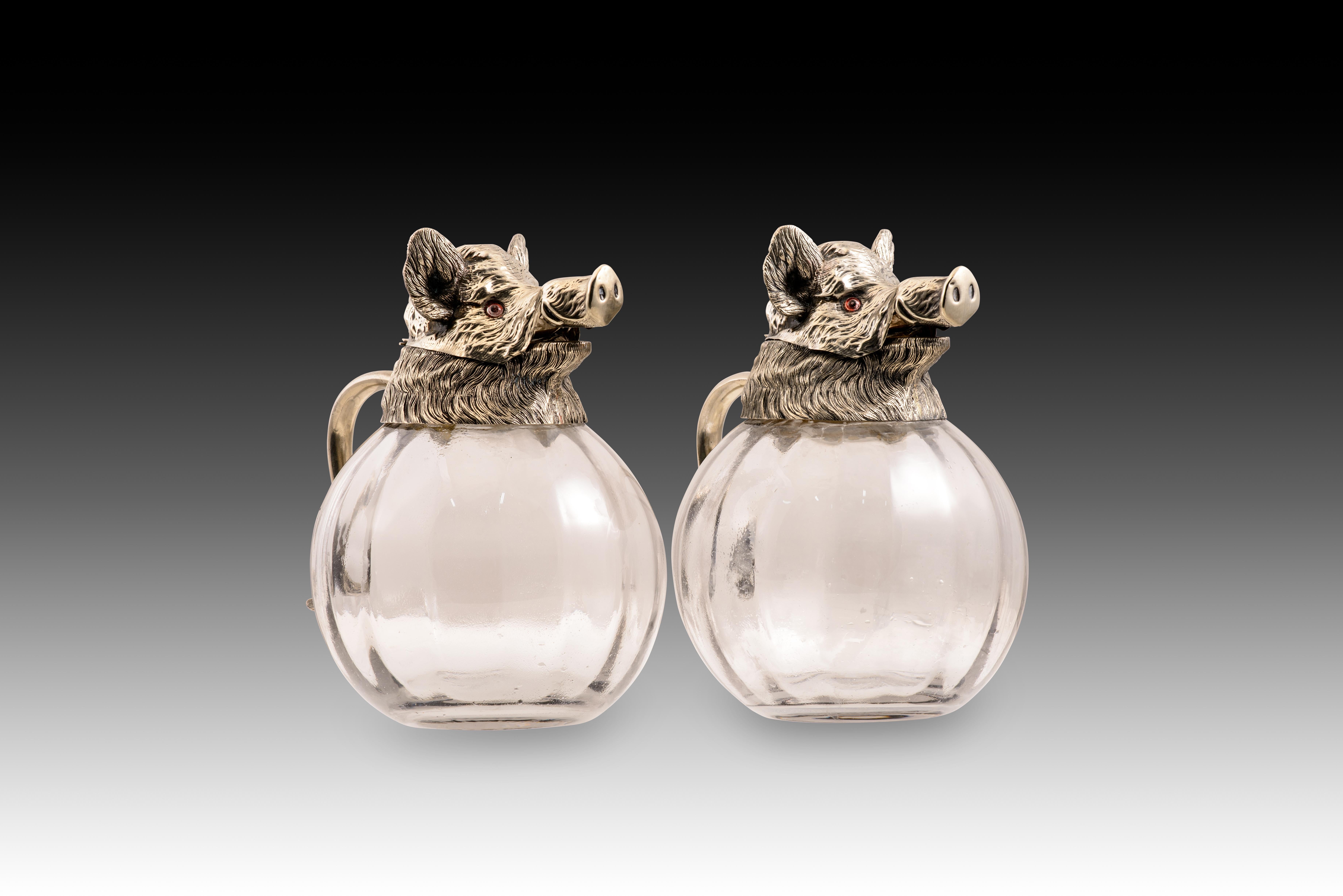  Paire de cruches, sangliers. Métal argenté, verre. Probablement Espagne, vers le milieu du XXe siècle, d'après des modèles de Valentí. 
Paire de pichets dont le corps en verre transparent est orné de spirales à l'extérieur et dont la pièce en métal