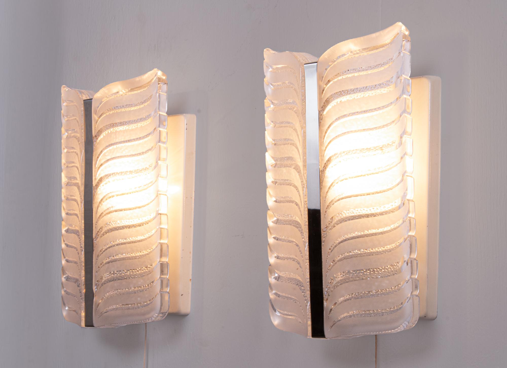 Elegante conjunto de dos grandes apliques de pared de grueso y pesado cristal de Murano con una pieza central cromada sobre un marco de metal blanco. Gema de la época. Con estas luces, puedes marcar una clara tendencia en tu diseño de interiores. Un