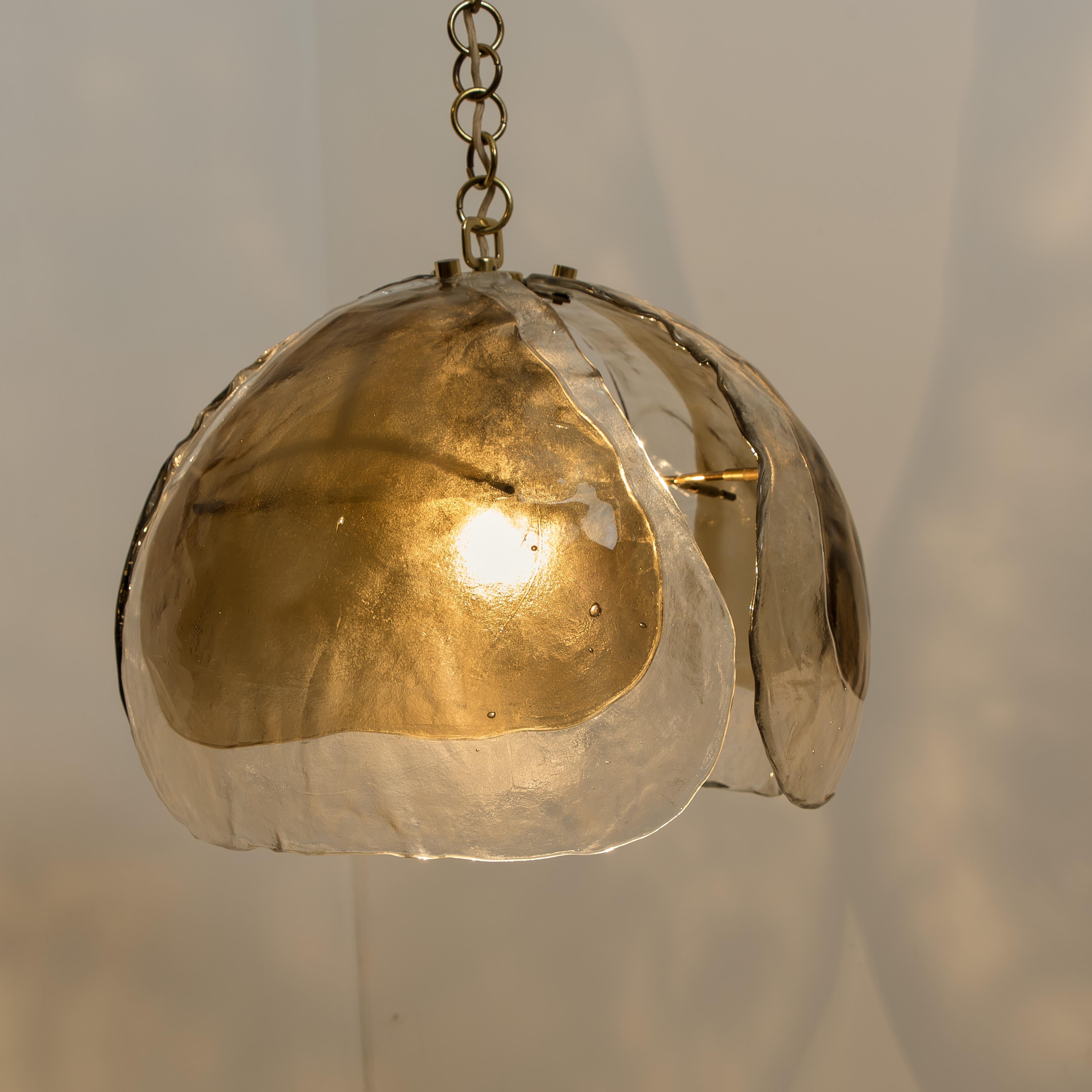 A nice pair of pendant lights in the style of Kalmar. Three smoked tone murano glasses are mounted on a brass fixture.
The hand blown leaves are refracting the light in a beautiful way. It fills the room with a soft, warm and welcoming