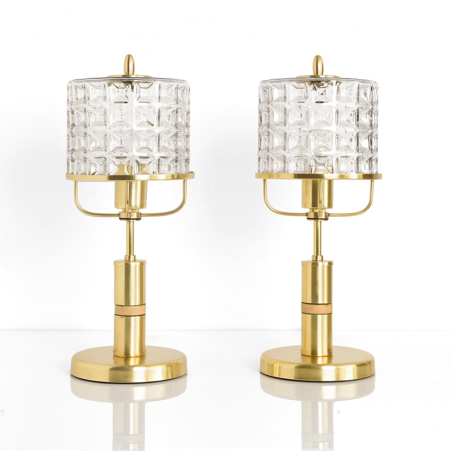 Pair of Kamenicky Senov mid-century Modern table lamps with brass plated steel frames. Each lamp has a single standard base socket and has been newly rewired for use in the USA. The clear glass shades have a 3 dimensional pattern and rest on a