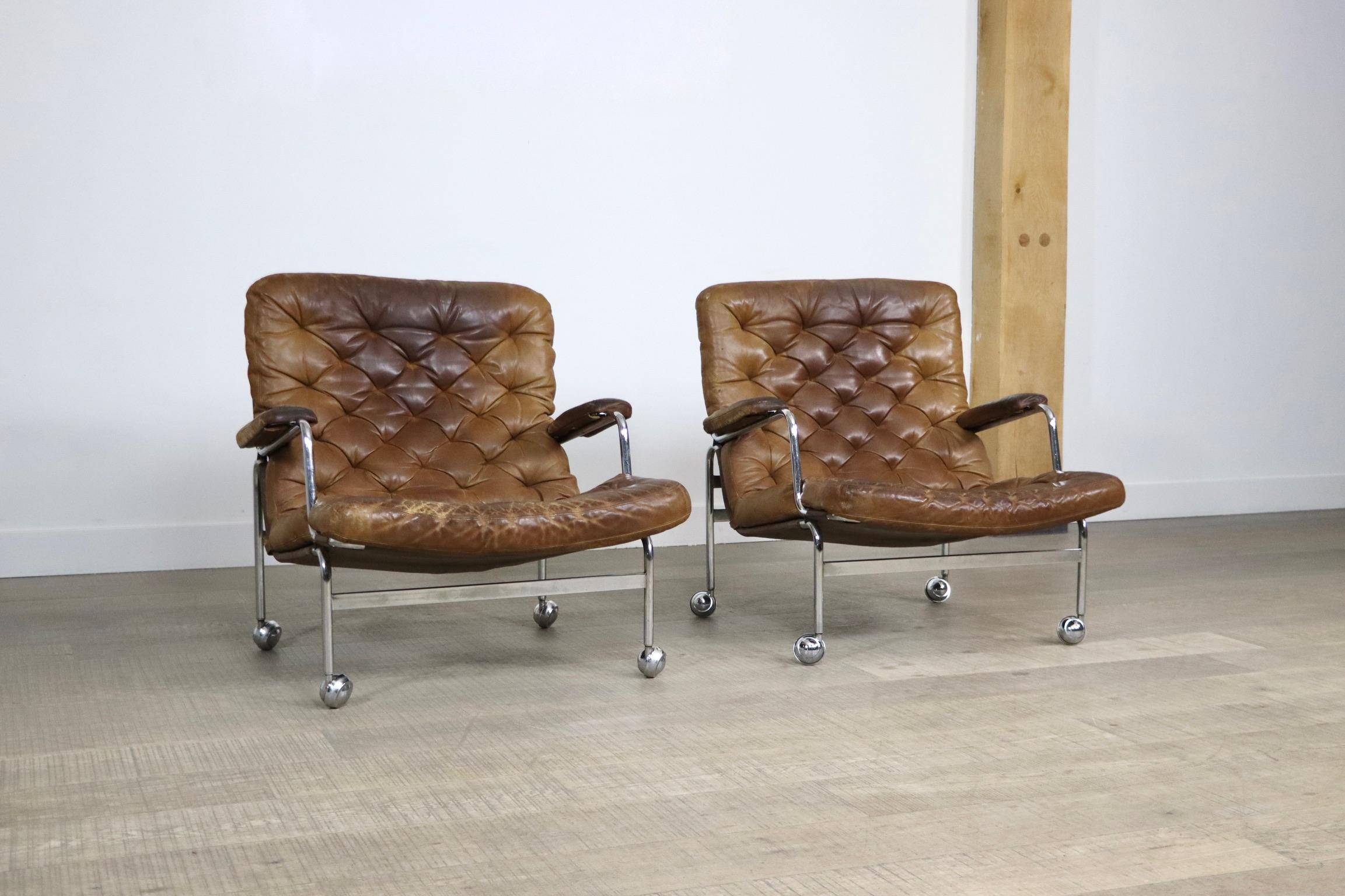 Amazing pair of Karin chairs in tan leather and chrome by Bruno Mathsson for Dux. 1970s. The highly comfortable minimalistic design will be the perfect addition to any seating area. The chrome wheels are besides a beautiful addition to the design