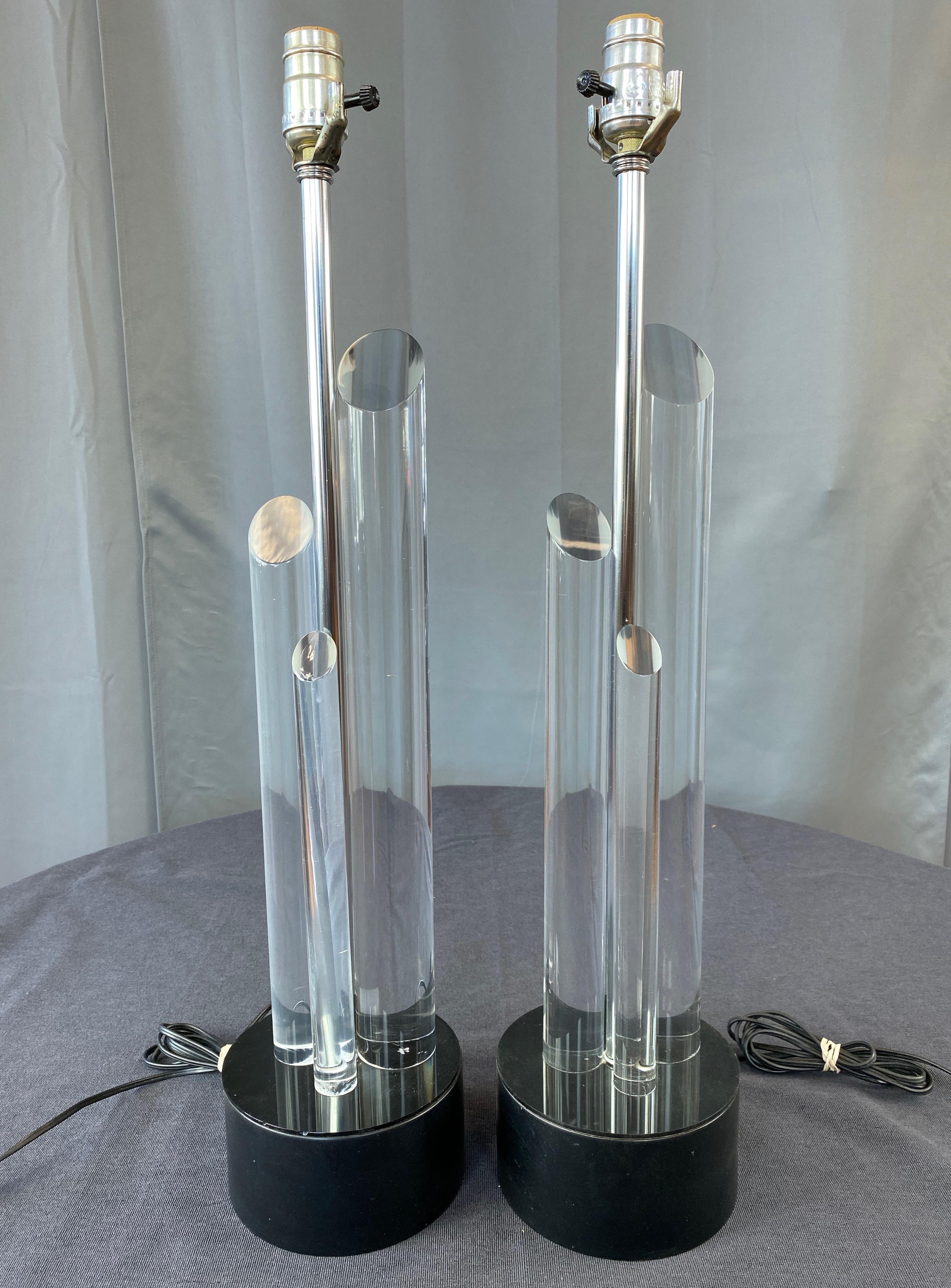 A pair of chic 1960s lucite table lamps on black metal bases done in the manner of Charles Hollis Jones.

Sculptural trio of lucite rods of graduated height and diameter on acrylic-capped matte black enameled cast aluminum base. Polished nickel stem