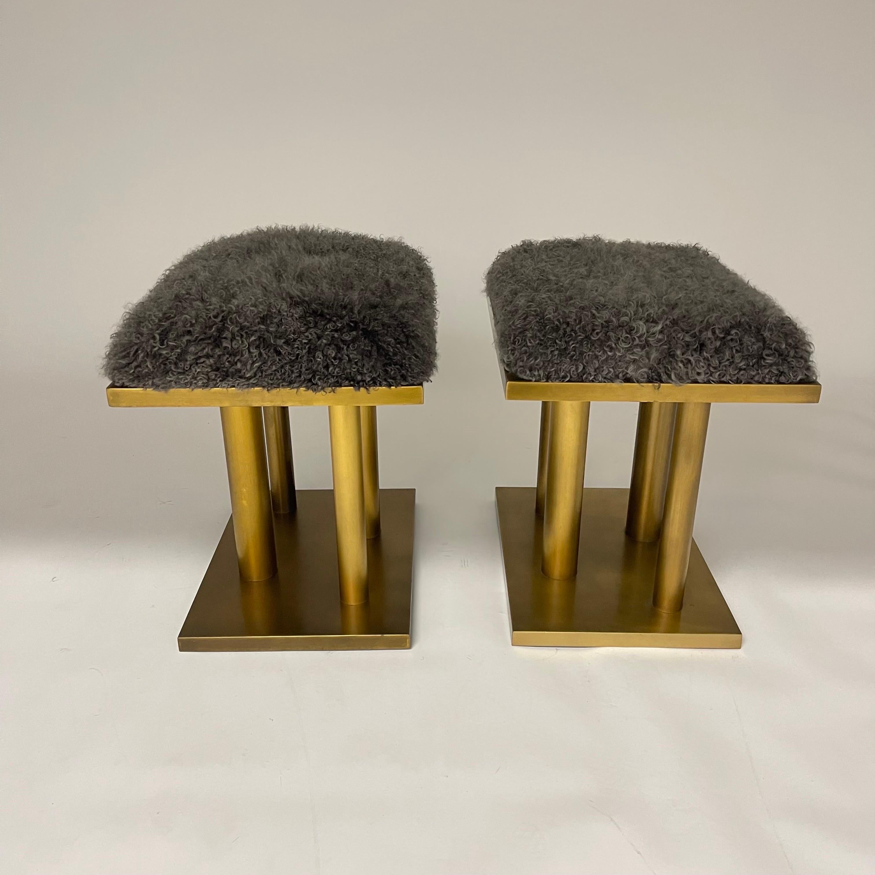 Pair of stunning stools or ottomans rendered in a heavy bronze patinated frame with upholstered seats in curly grey Mongolian lamb hide with adjustable feet.  Designed by Kelly Wearstler still retaining tags. USA 2015