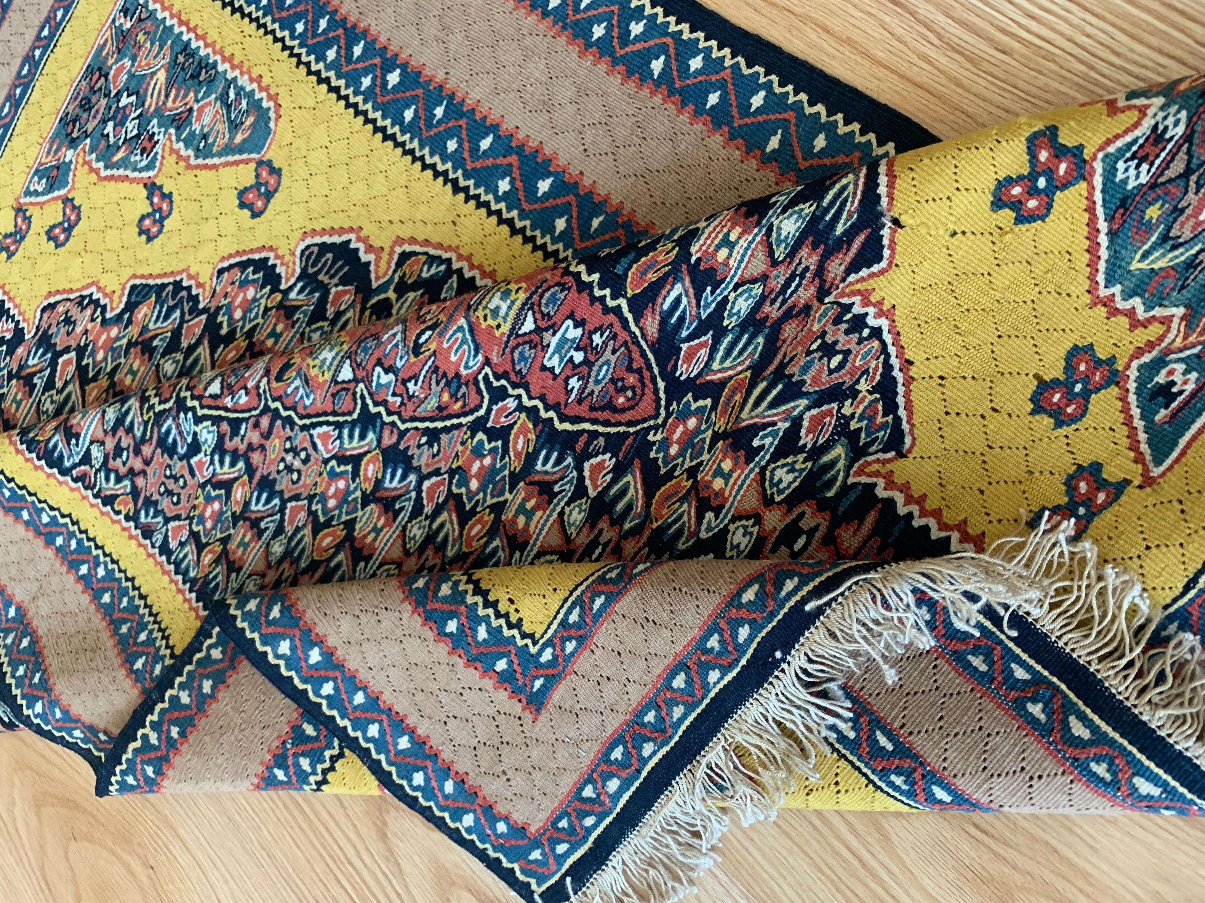 These bold yellow rugs area a pair of handmade flatwoven kilim rugs, construected in the early 2000s. The central design has been oven on a yellow background with a large medallion woven in accents of rust, blue and green that make up the intricate