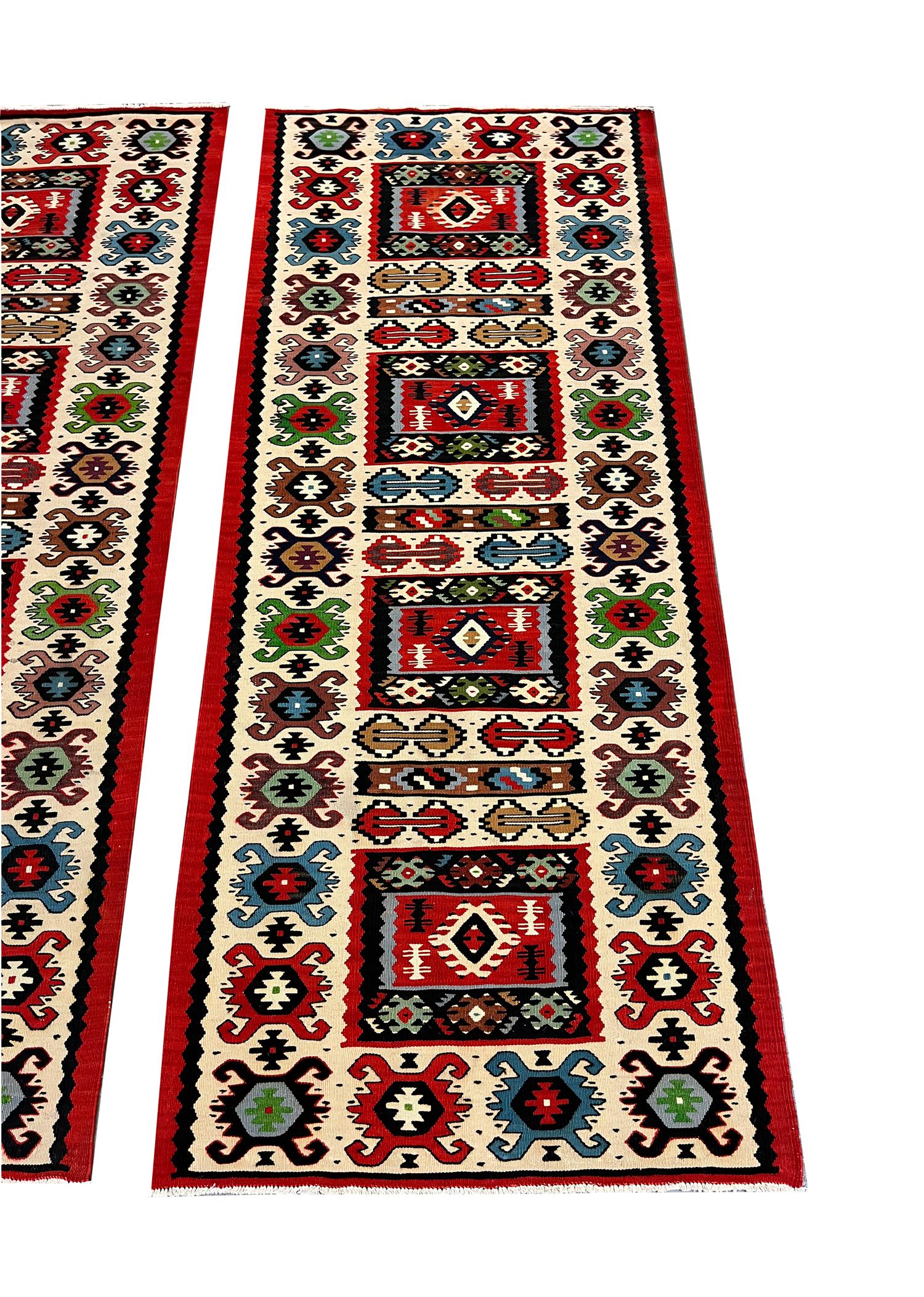 These Kilim runner rugs are fantastic examples of rugs woven in Turkey in the 1970s. The design features a layered repeating pattern woven on a cream background with accents of red, green, blue, beige and brown. The colour palette and the design