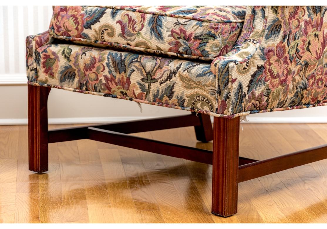 A pair of Kindel upholstered wing chairs covered in multi-color woven tapestry-like fabric. The chairs with roll arms, beautifully upholstered with piping throughout, having fluted mahogany front legs, gently splayed back legs and supported with an