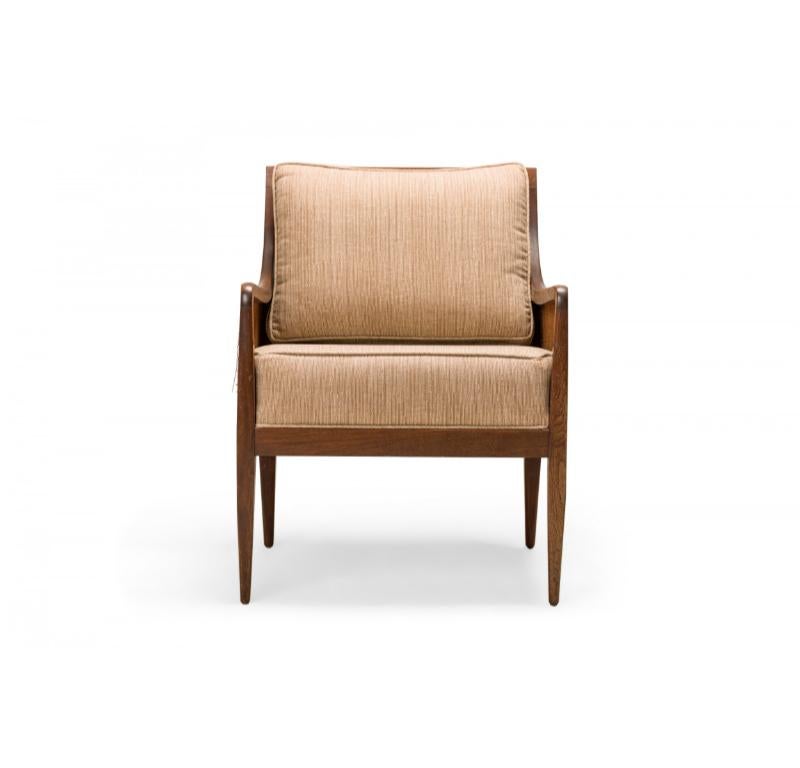 PAIR of American Mid-Century lounge armchairs / bergeres with walnut frames, caned sides and backs, and seat and back cushions upholstered with a beige fabric with a light stripe pattern, resting on four tapered square walnut legs. (KIPP STEWART FOR