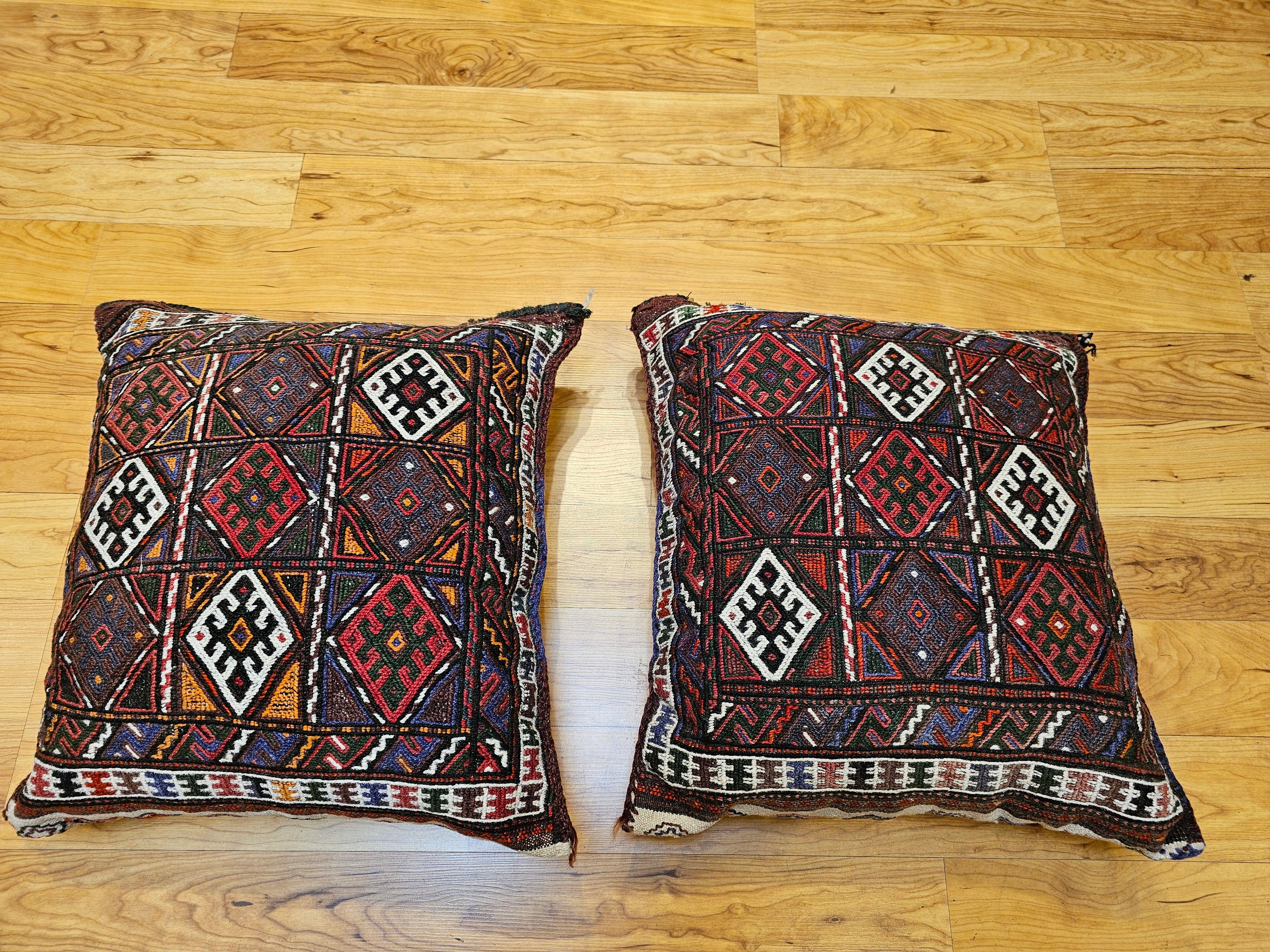 Pair of beautiful hand sewn pillows made from antique Kurdish saddlebags that were made in the early 1900s. Each pillow has a hand knotted rug with a geometric 3 x 3 star design for the face of the pillow in red, ivory, green, and purple.  The back
