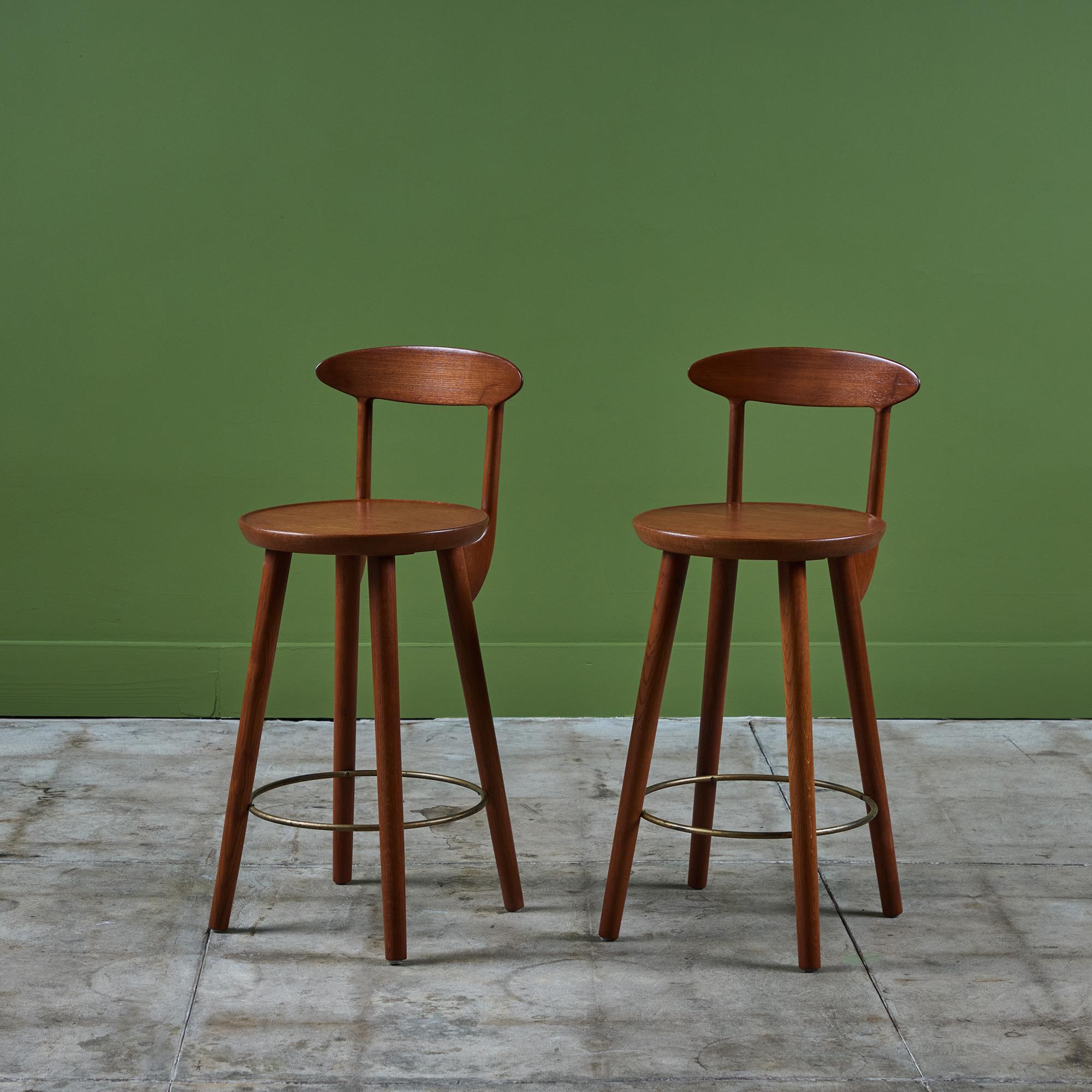 Pair of teak stools by Danish born designer Kurt Østervig for Brande Mobelindustri, c.1960s, Denmark. The stools feature a round seat and curved seat back. Each stool has four long splayed legs with a circular brass foot bar.

Dimensions
14
