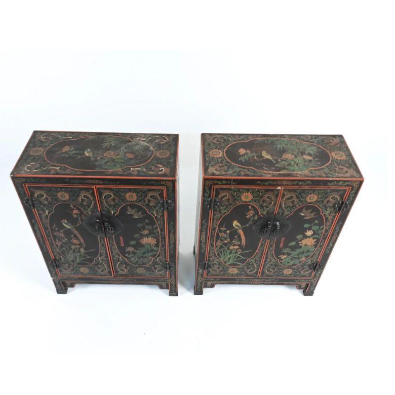 Una coppia di armadietti a cineserie in lacca nera, ciascuno con due ante e un ripiano interno. Gli armadi sono decorati con motivi asiatici di draghi, uccelli, viti e fiori con bordi rossi e decorazioni in verde, oro e marrone.