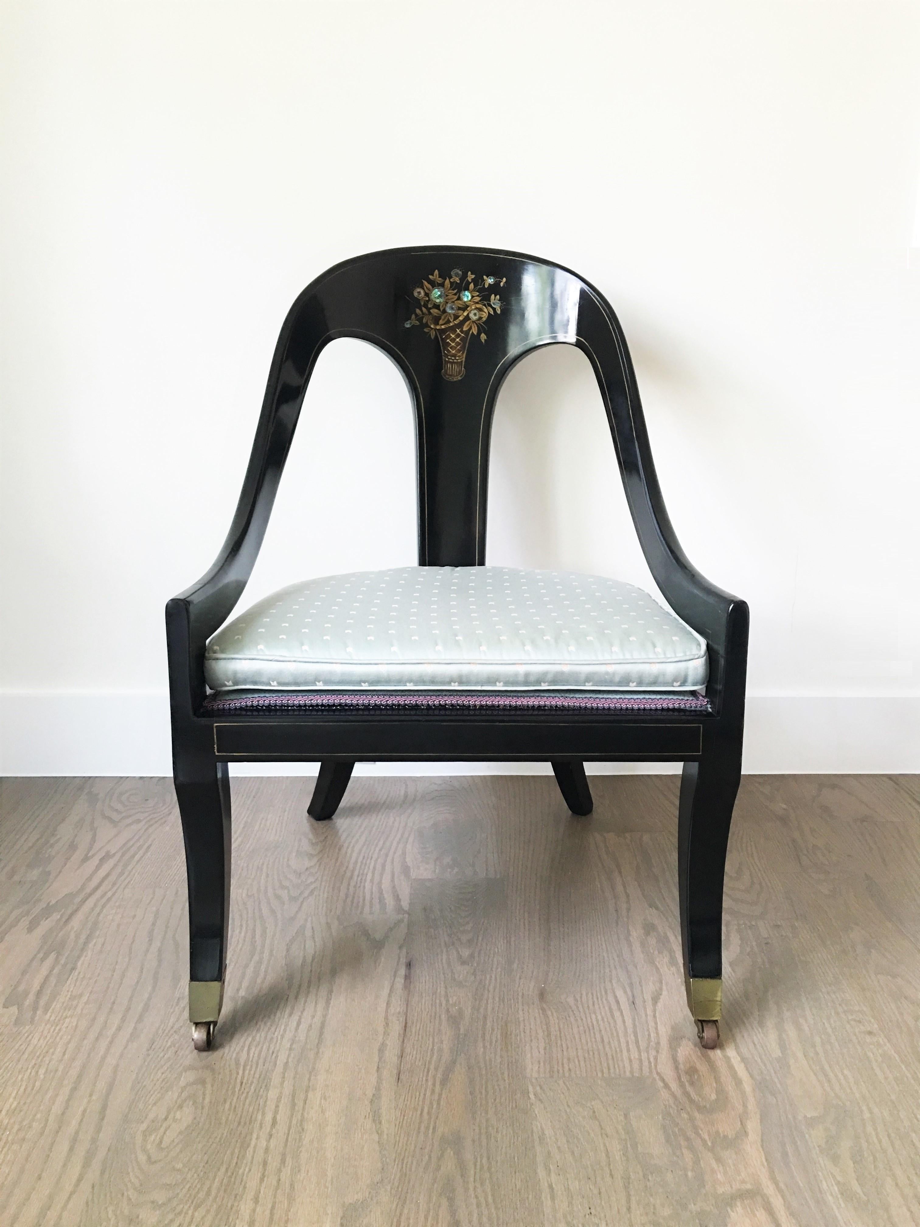 Pair of Regency style spoon-back chairs. The chairs have black lacquered frames featuring an arched crest above a vertical splat with a floral mother of pearl inlay pattern flanked by down swept arms. Hand decorated with gilt detailing, upholstered