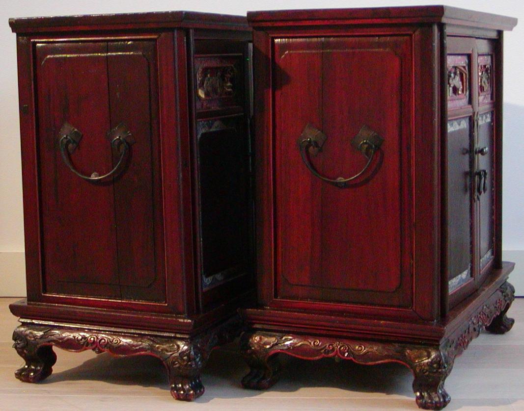 A pair of Chinese bedside cabinets of red lacquered soft wood, each cabinet with a set of doors ornamented with glass and shell inlay, a gilt relief carving depicting scholars above and painted panels depicting floral scenes below, each opening to