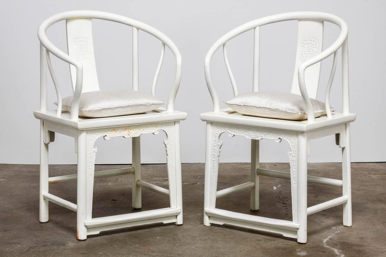 Stylish pair of white lacquered Chinese horseshoe armchairs made in the Ming style. Featuring a decorative carved back splat with two dragons and carved front aprons. The chairs have a thick lacquered finish and are supported by round legs with