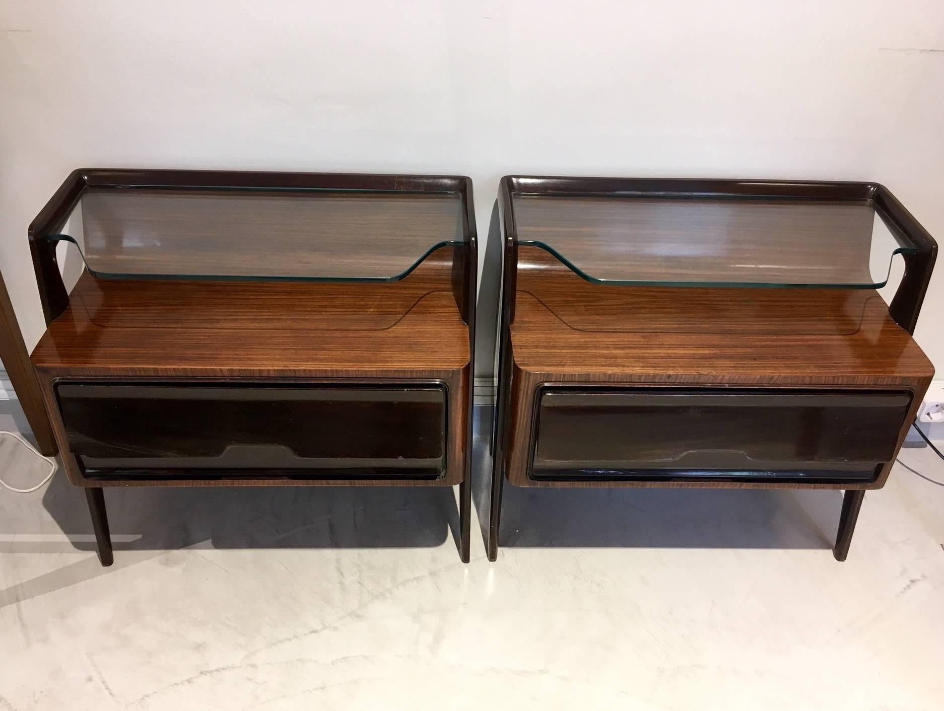 Pair of bedside tables attributed to Paolo Buffa (1903-1970), Italy, circa 1950. Wood lacquered and lined with kingwood, top and shelf in glass. Drop-down doors. One nightstand is missing a door hinge. Some age-related wear.