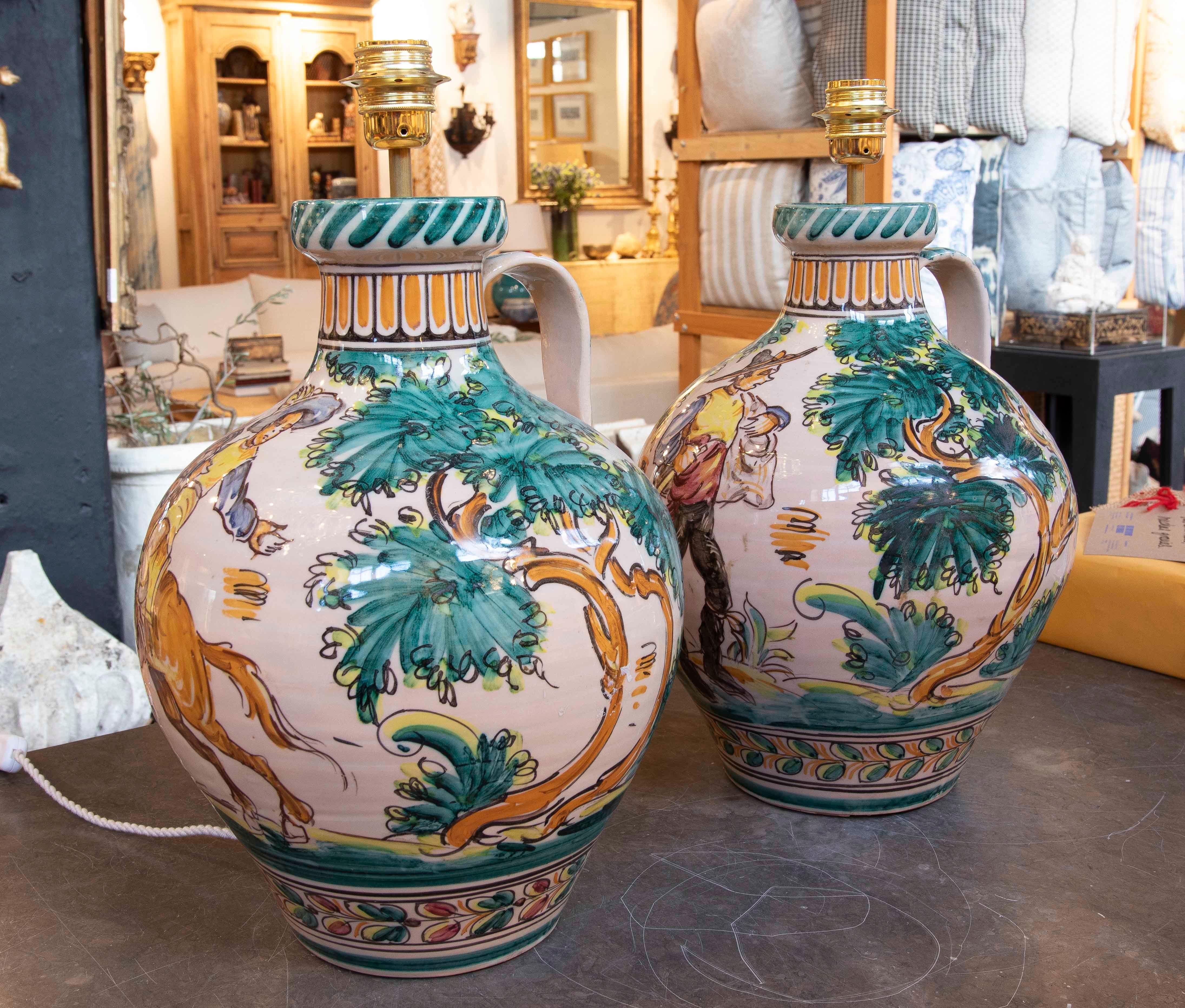 Pair of ceramic lamp bases with hand-painted motifs depicting trees and foliage in green and gold tones. Their design incorporates traditional Mediterranean elements, highlighting ornamental details at the top and bottom. Each base includes a