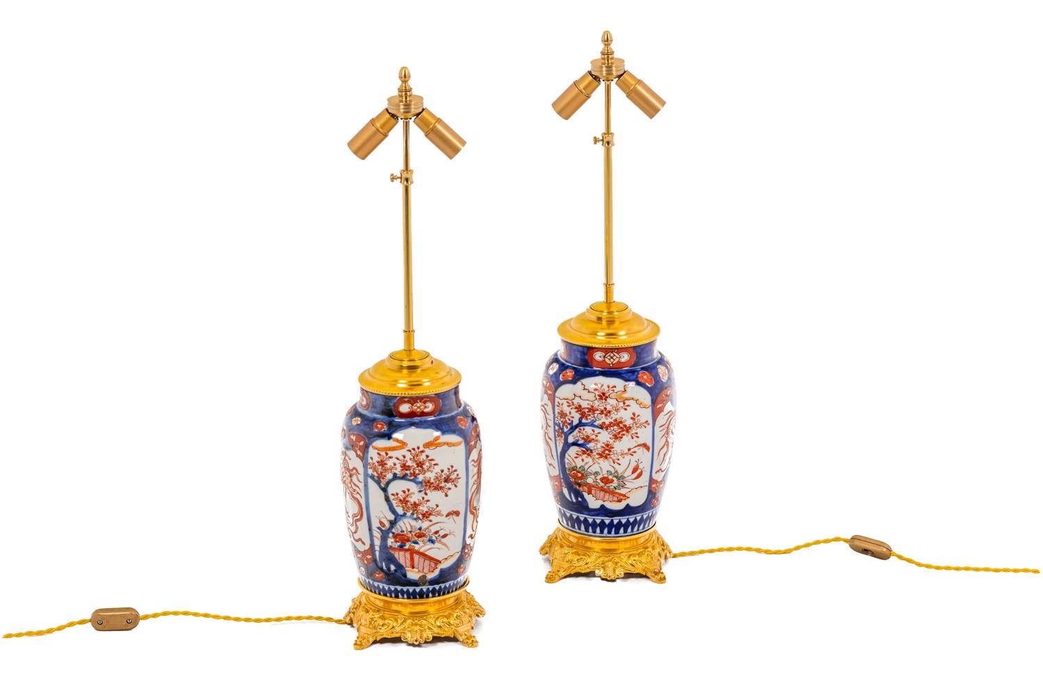 Pair of egg-shaped lamp with red, blue and white Imari decor topped by a neck presenting a decor of branches of cherry tree and blue and red phoenix in white-backgrounded reserves. The porcelain is sealed by a lid and a base in gilt bronze adorned