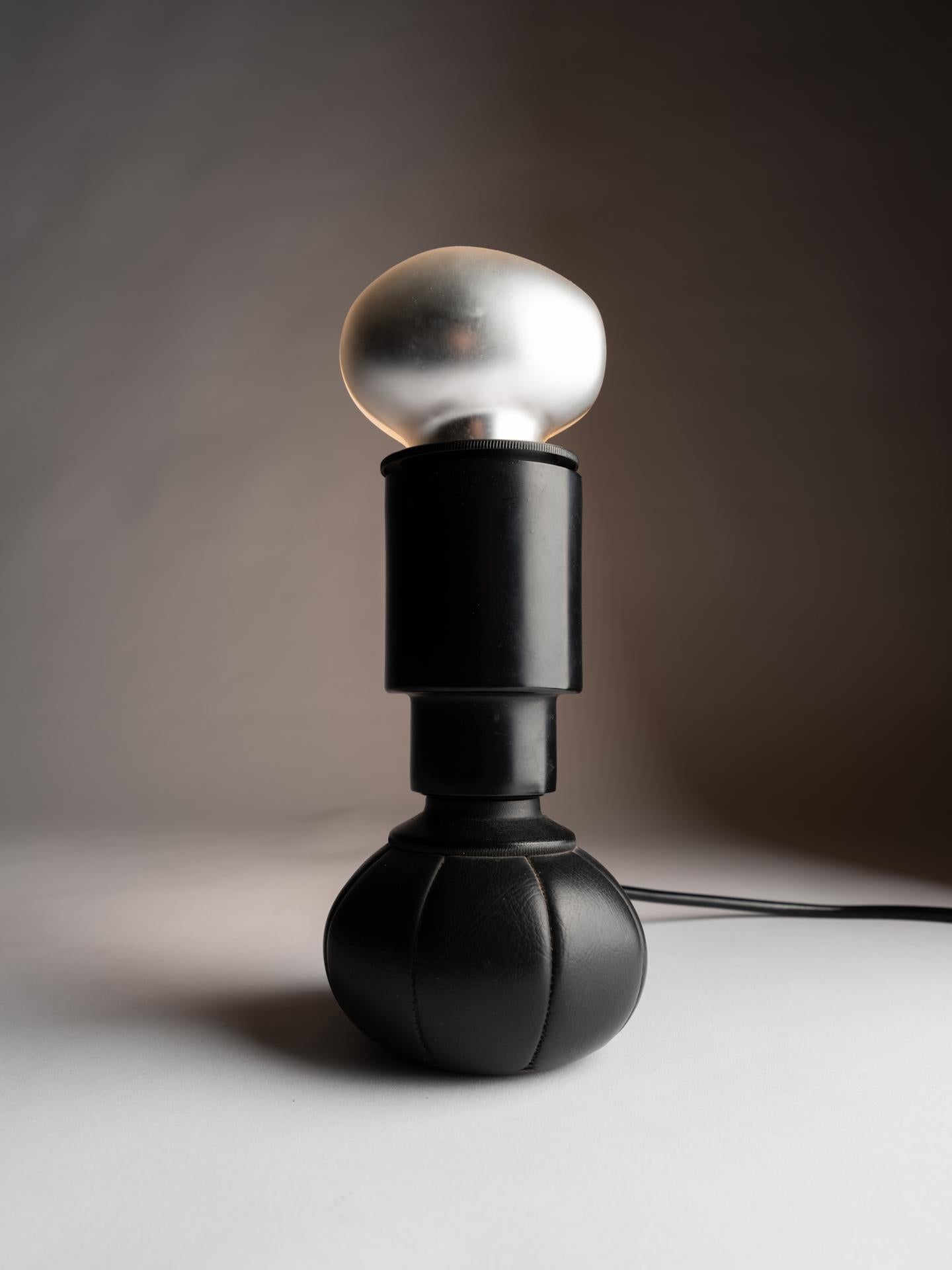 The 600C table lamp was designed by one of the greatest lighting designers of the 20th century Gino Sarfatti in 1966 for Arteluce Italy. 
It is made of black lacquered aluminum and it has a leather pouch filled with lead shot at the base . The type