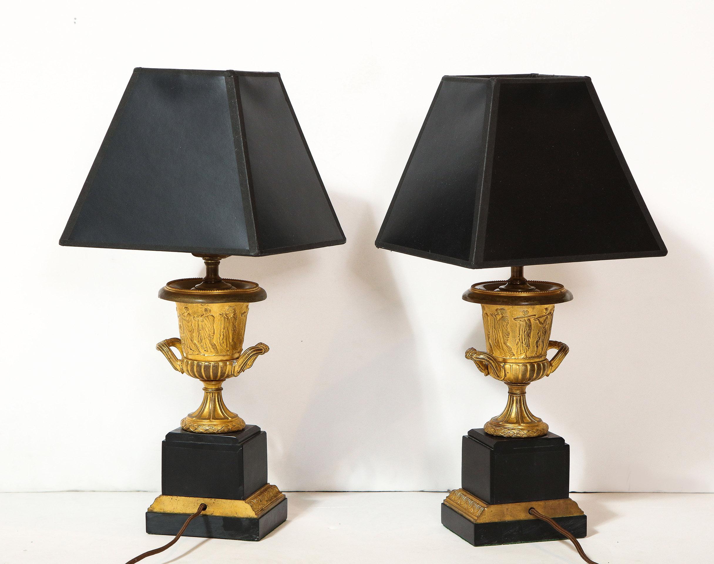 Pair of French Empire style bronze urns converted to lamps. The doré bronze urns with embossed neoclassic motifs on black marble bases.

The lamps have been recently wired.