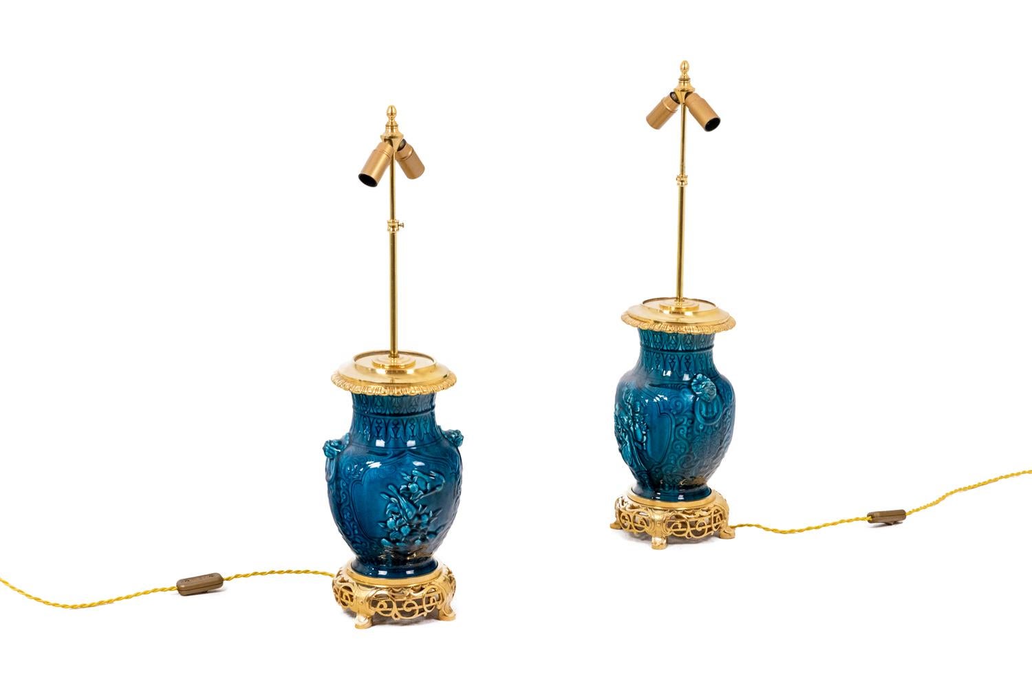 Coppia di lampade in inceramica e bronzo dorato, di colore blu, ornate da foglie in rilievo, con anello ornato nella parte superiore. Base in bronzo dorato, cesellata e traforata con intrecci. La parte superiore della cornice è ornata da