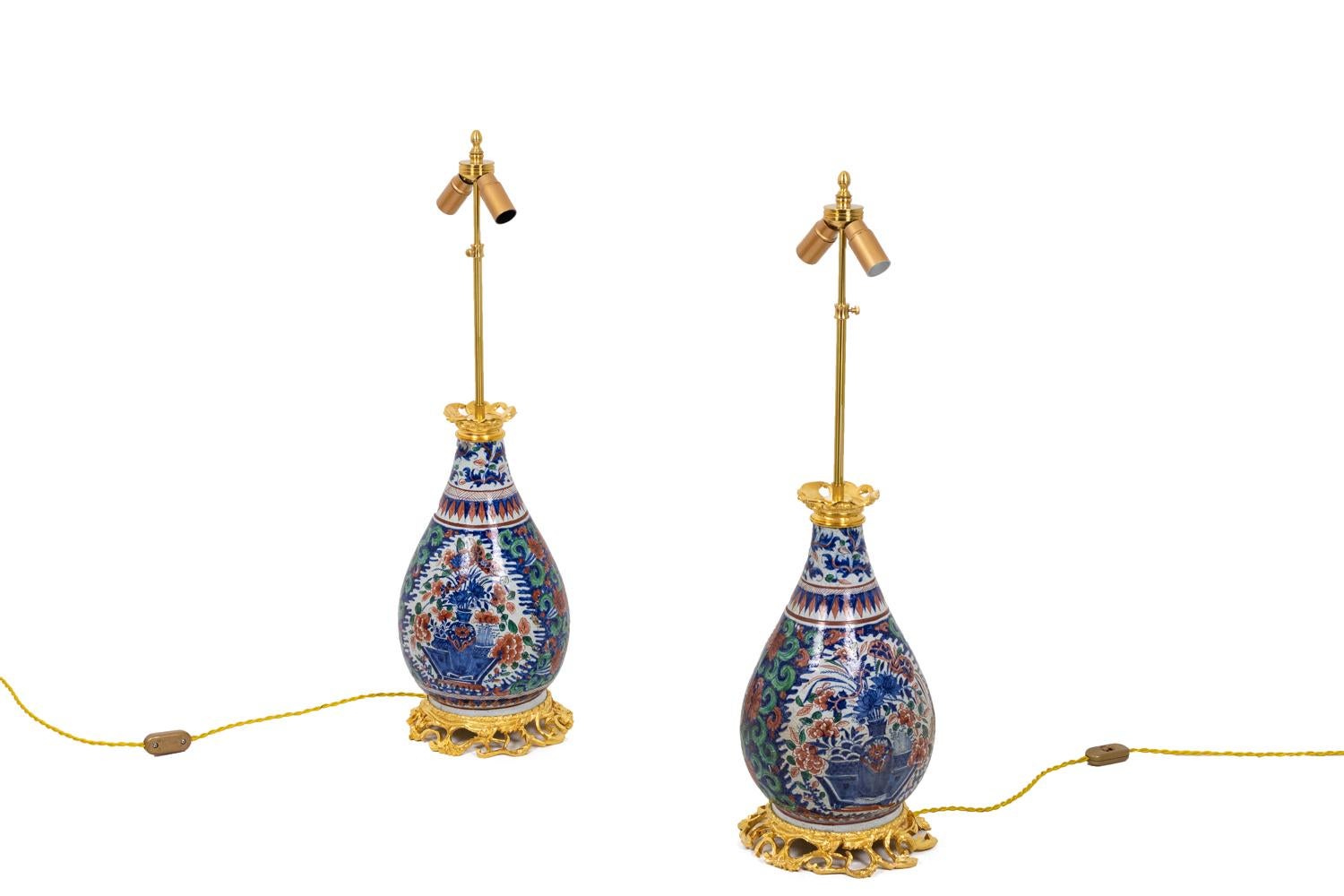 Baluster shape lamp in Delftware and gilt bronze. Shaft adorned with two large cartouches framing red peonies bouquets in vases on a blue background adorned with vegetal green and red scrolls. Neck and foot adorned geometrical blue an red strips.