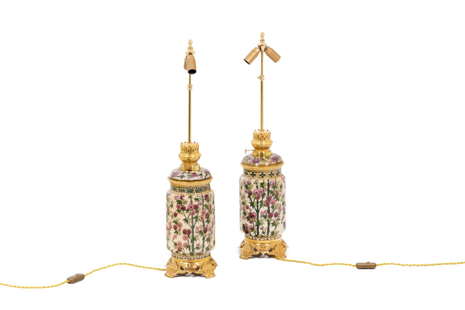 Pair of lamps in enamelled earthenware, ovoid in shape and adorned with branches and cherry blossoms, green and pink on a white background. Frame in chased and gilded bronze. Quadripod base. One of the two lamps is signed Kosmos Brenner on the