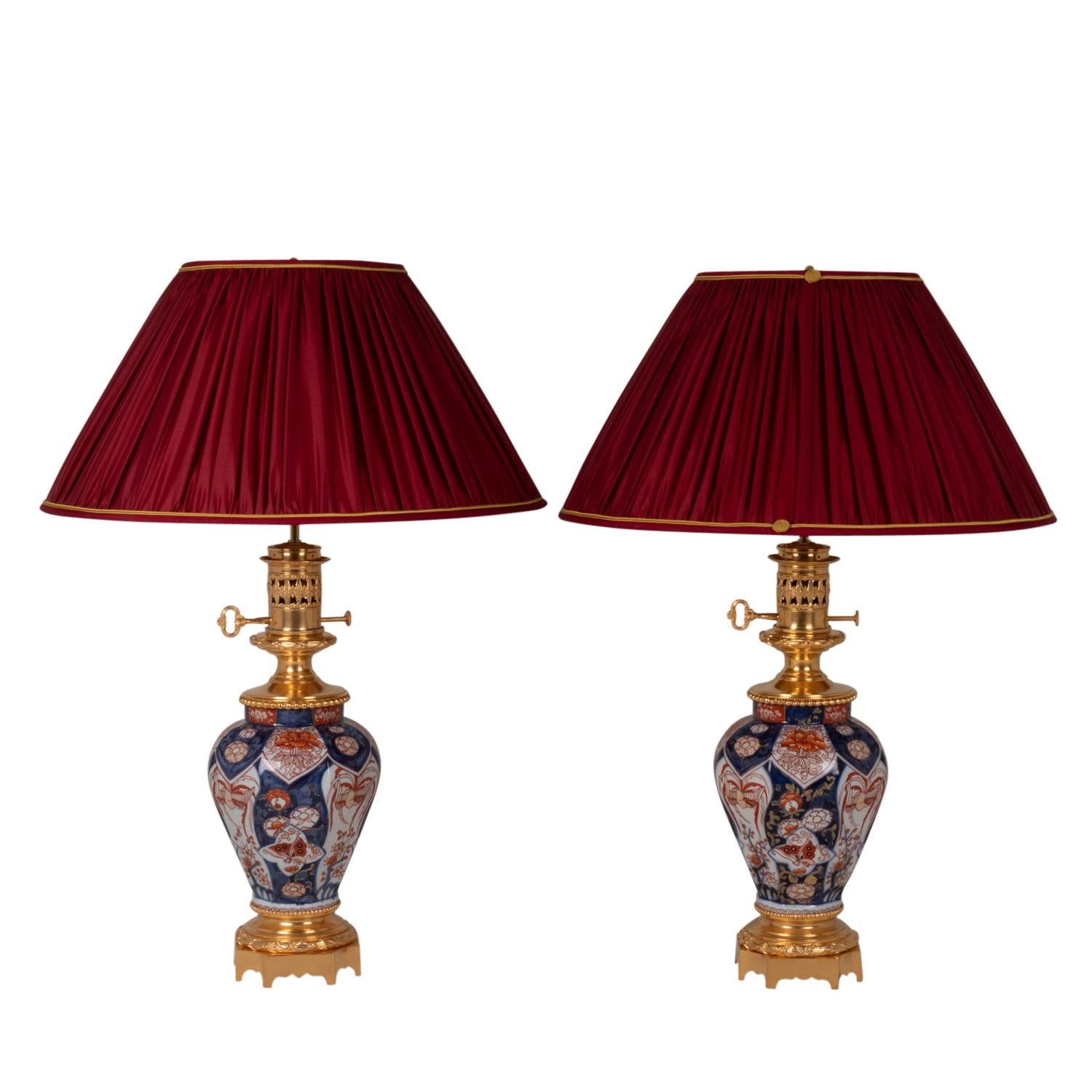 Pair of lamps in Imari porcelain and bronze, adorned with flowers and leaves, in shades of cobalt blue, saffron red and porcelain white. Square base with four concave angles. Top of the frame with pearl decoration and a key.

French work realized