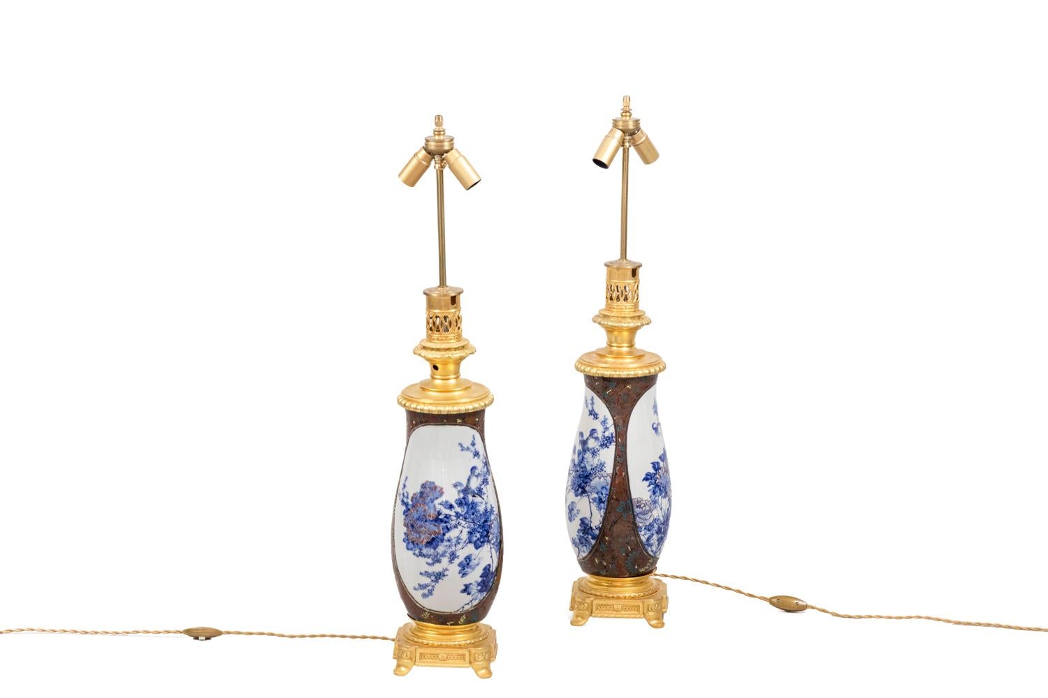 Paire de lampes en porcelaine japonaise en forme de vase.
Décor sur fond brun et motifs stylisés de fleurs, de feuillages et d'oiseaux dans les tons bleu, jaune et rouge. Deux grands cartouches à fond blanc avec un décor bleu figurant des pivoines,