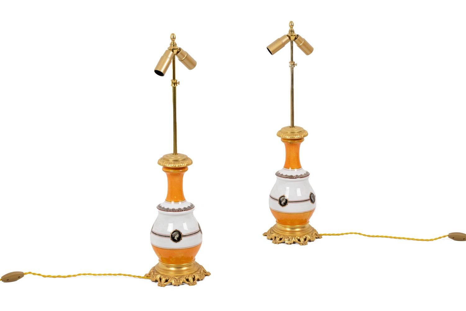 Paar balusterförmige Lampen mit einer kleinen Ausbuchtung in orange und weißem Porzellan. Dekor aus Perlenfries und geometrischen Motiven auf dem Hals, Medaillons mit Profilköpfen im griechischen Stil auf dem Bauch, die durch Gitter miteinander