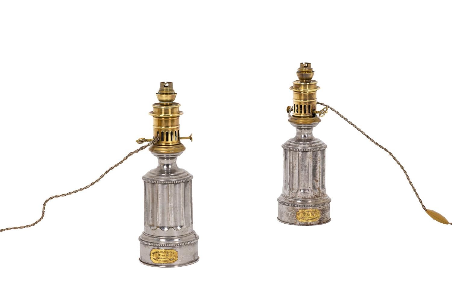 Pair of lamps in tin with a fluted shaft. Decor of frieze of beads on the base and the top of the mount. Gilt cartouche embedded on the base mentioning 