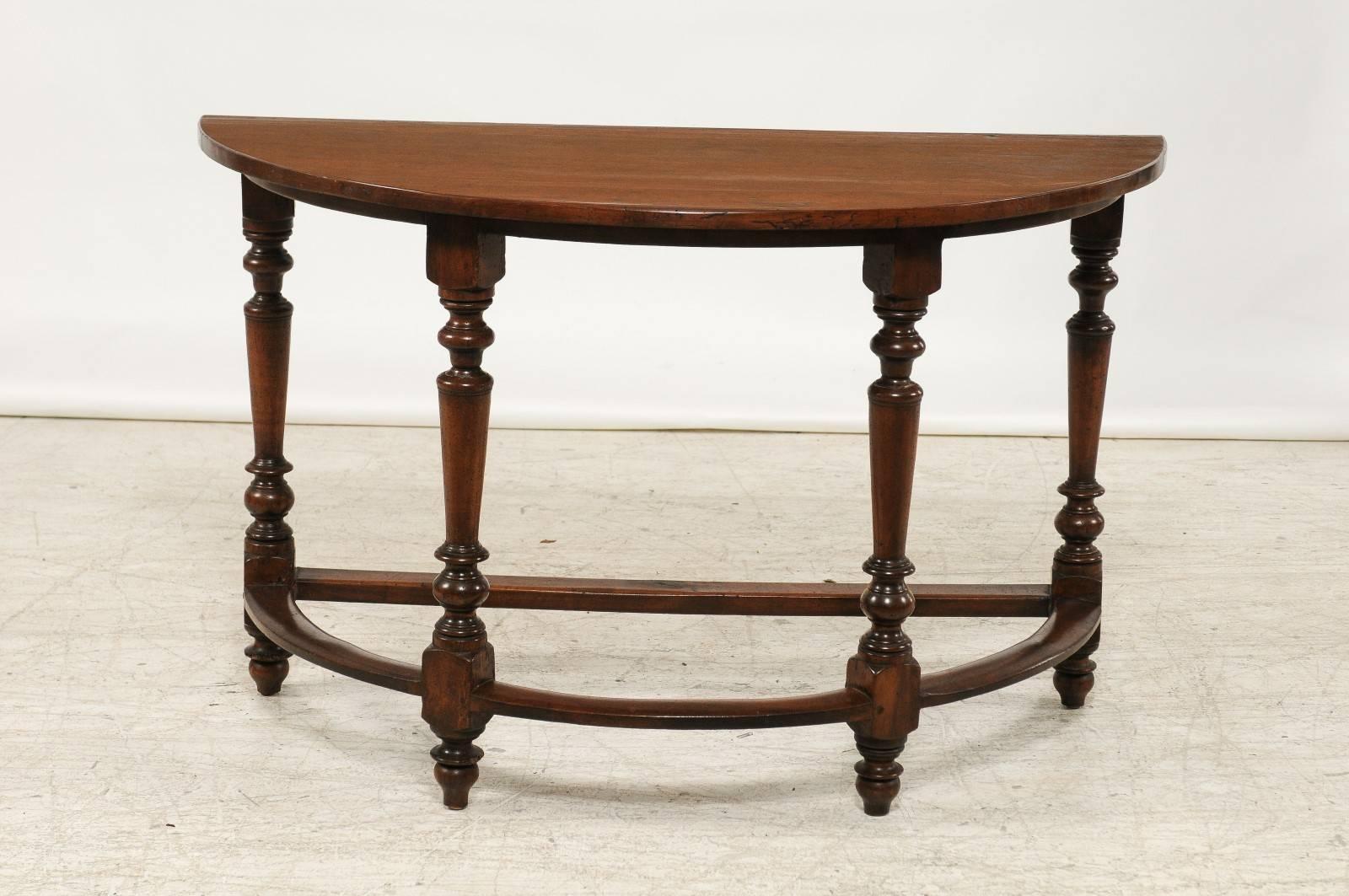 A pair of Italian walnut demilune console tables with turned legs and side stretchers from the early 19th century. Each of this pair of Italian demilunes features a semi-circular top, sitting above four elegantly turned legs with square block