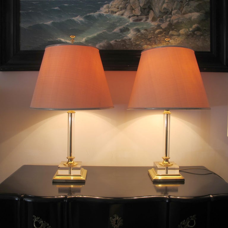 A large pair of Italian lucite and brass table lamps with their original shades, in great condition. This is a timeless elegant design; the lamps are presented on a brass base with a thick lucite/acrylic square and a tubular stem. The cream shades