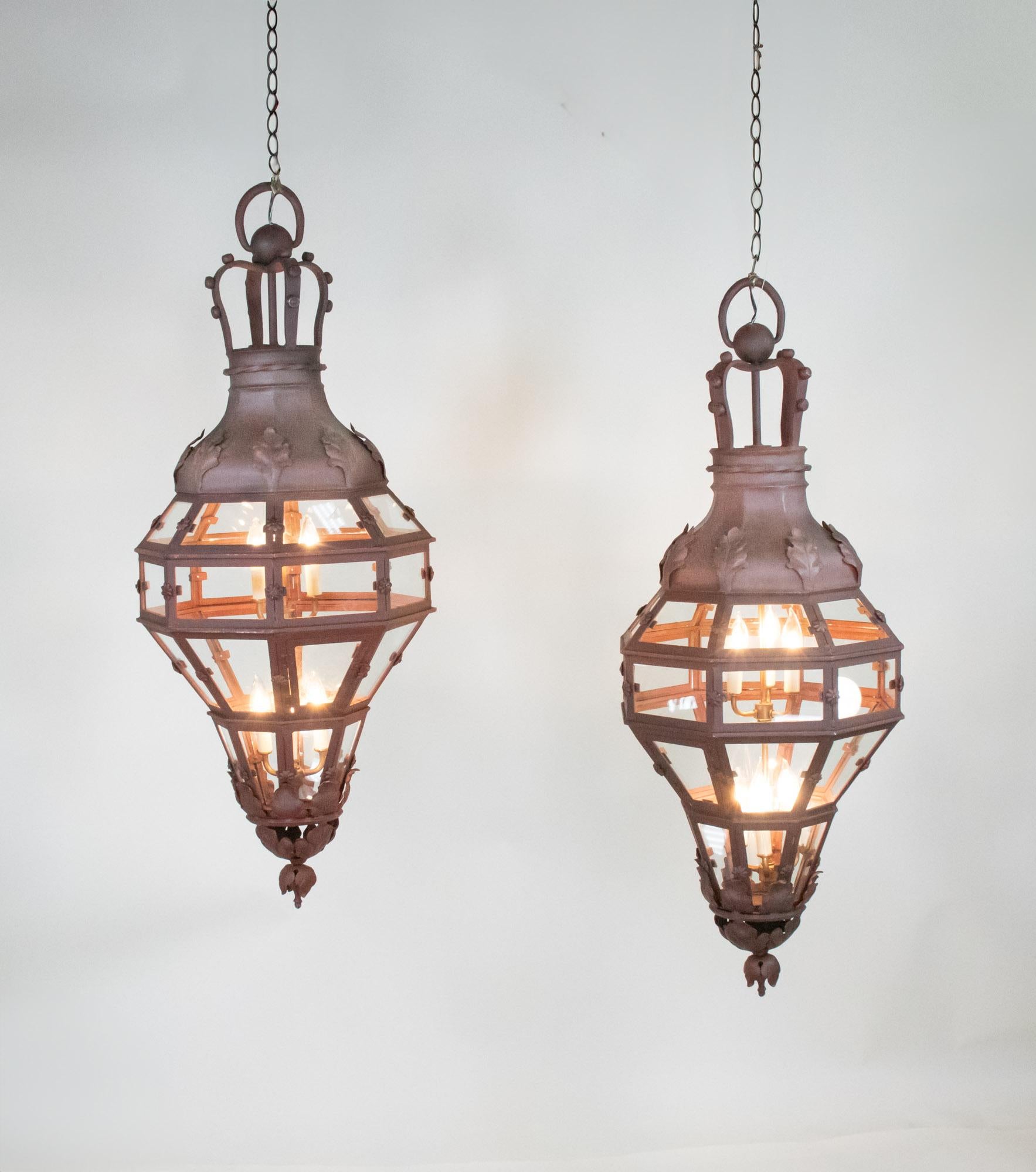 An exquisite pair of French 19th/20th century Louis XVI patinated wrought-iron and glass lanterns, with a warm reddish brown hue. This style was inspired by the last King of France, Louis XVI, and was characterized by classical ornamentation and a