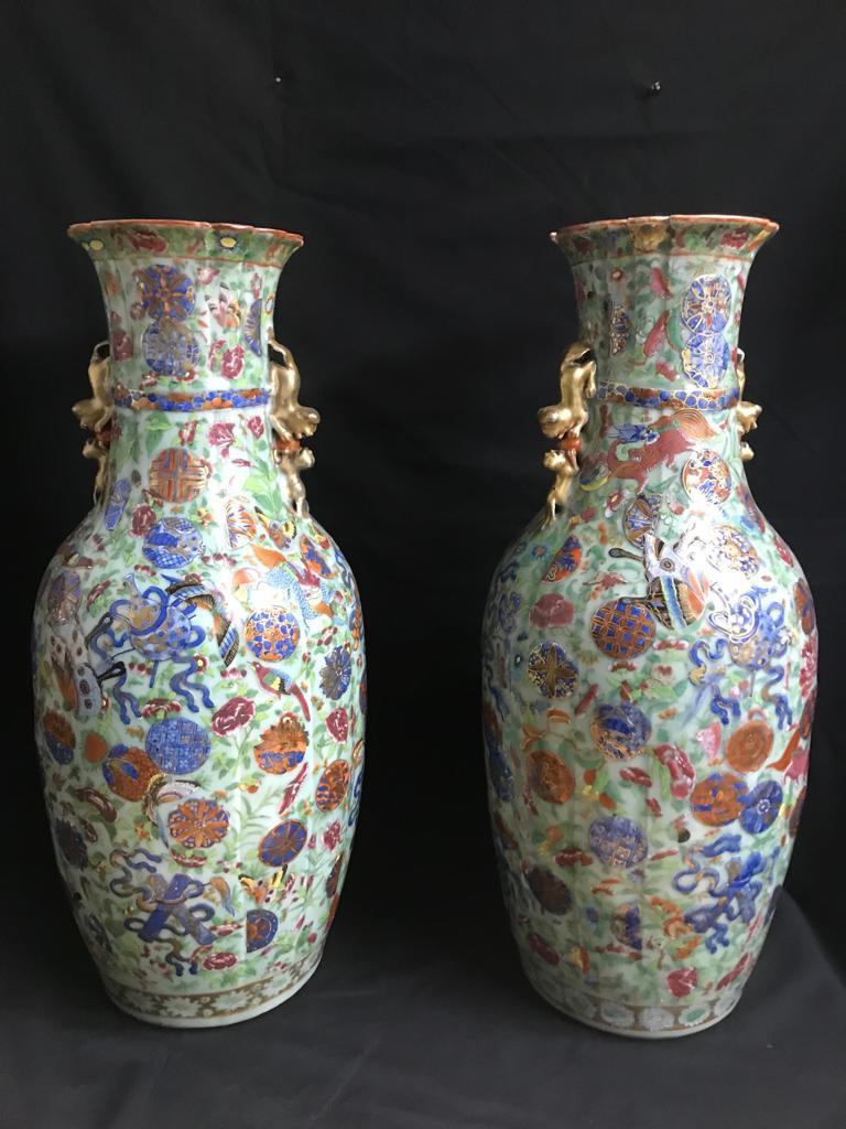 A pair of 19th century Chinese vases having multi colored and layered glaze. Hand-painted with intricate detail depicting Chinese symbols, flowers, foliage and butterfly's. The vases are flanked with gold lion handles on the tapered necks leading to