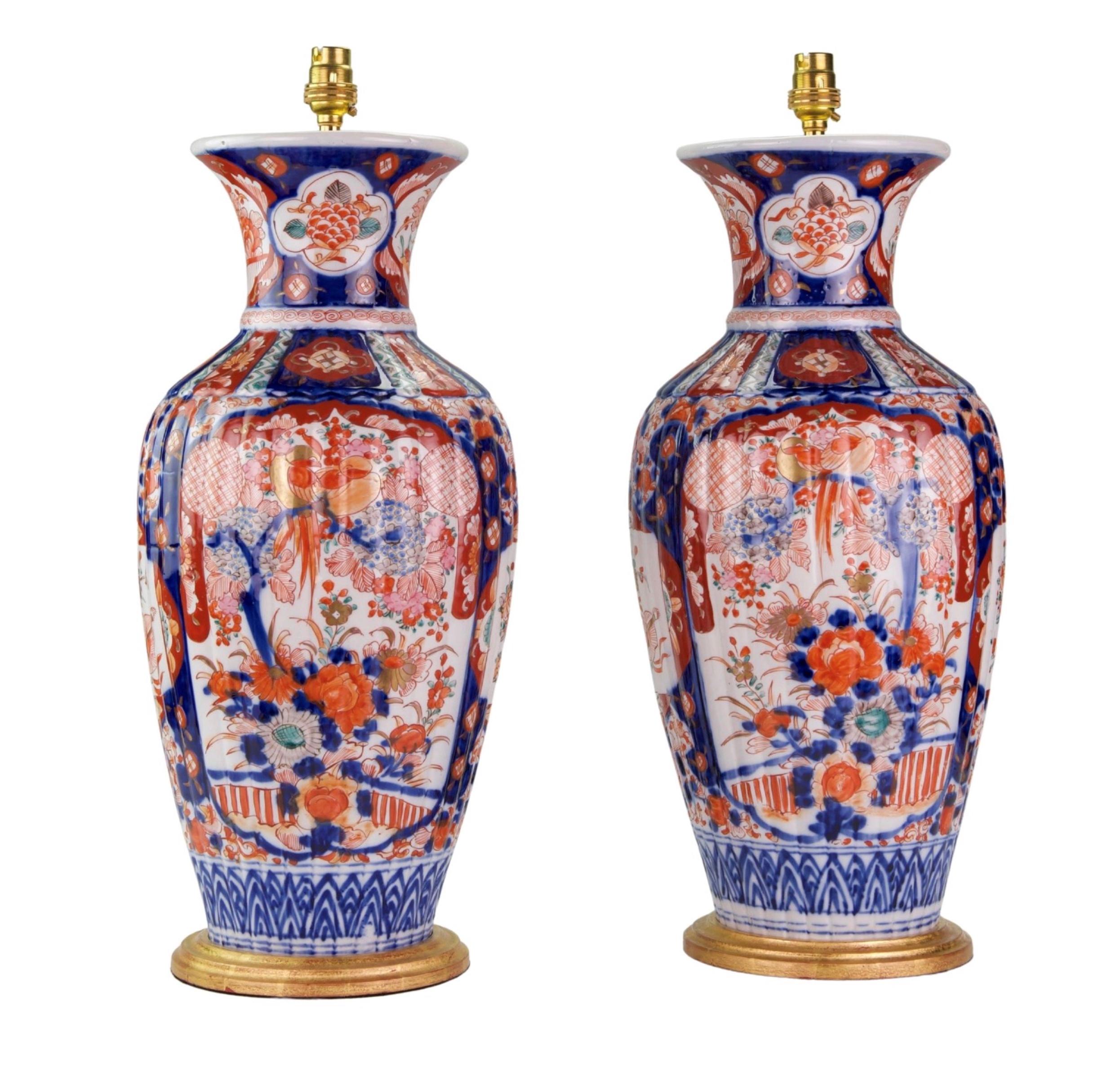 A fine pair of large Japanese Imari porcelain baluster vases, the ribbed bodies decorated in the typical Imari palette of blues, iron red and reds on a white background with central panels with a flowering tree in a garden landscape, surrounded by