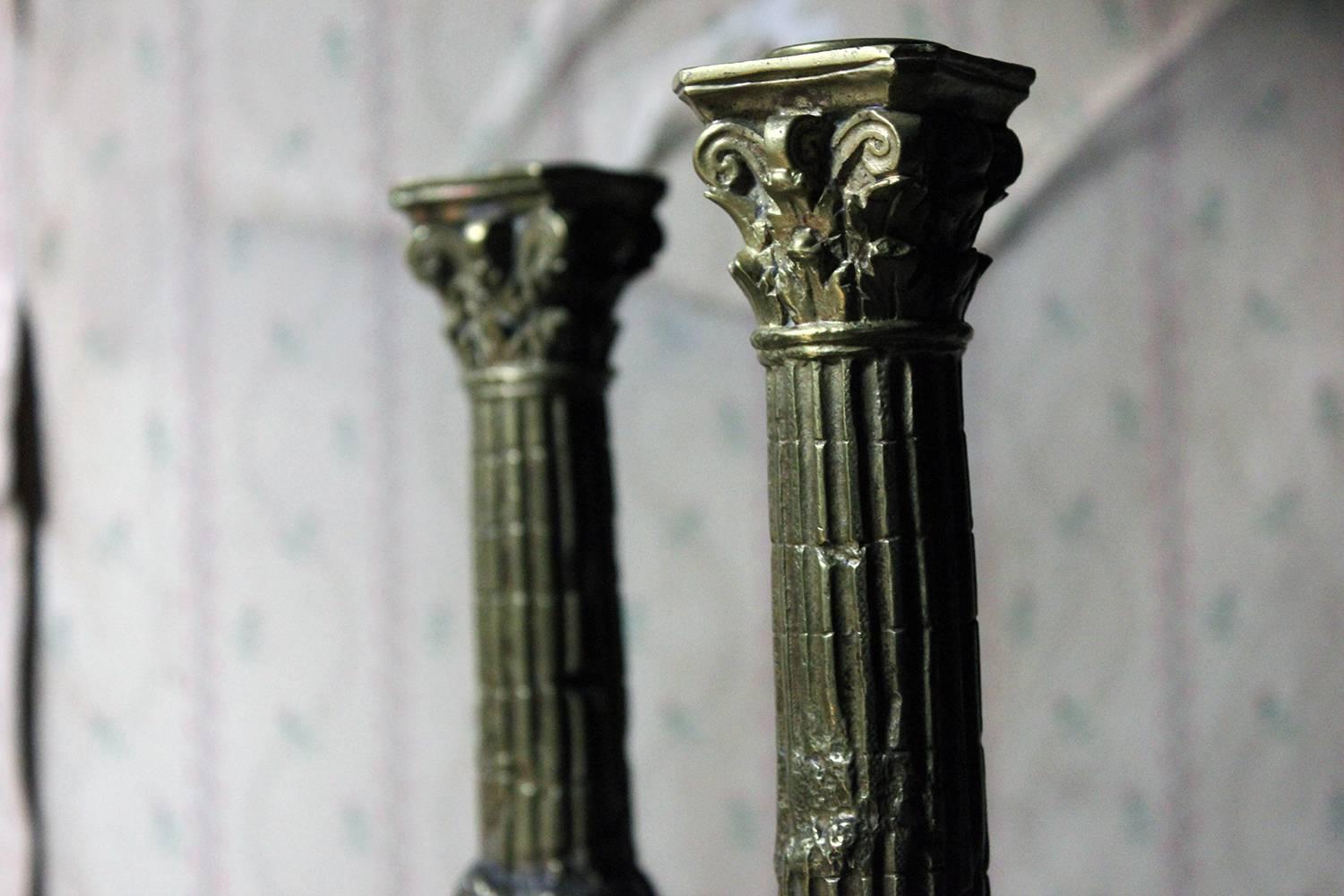 Of large proportions, the ormolu cast brass candlesticks fashioned as weathered Greek ruins in the form of fluted Corinthian columns on oblong plinths, each cast with masonry and plants within lappet borders, one being stamped '1245' to the inner