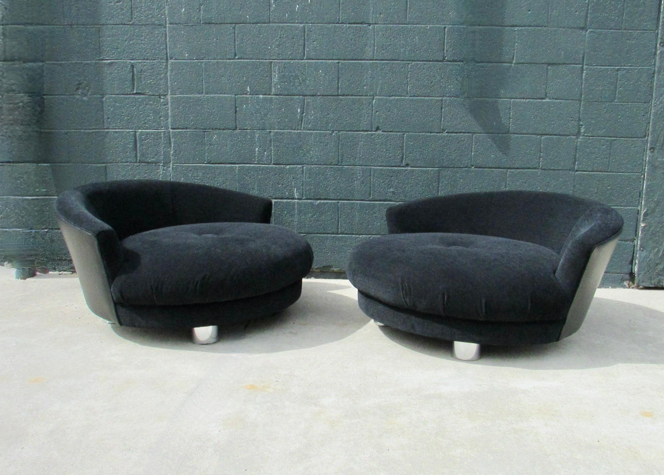 Large and inviting round lounge chairs. Perfect for partners to curl up in. Seat and backrest covered in black chenille backside done in black naugahyde. One center button tuft to seat. All sit on walnut legs wrapped in polished aluminum. Chair