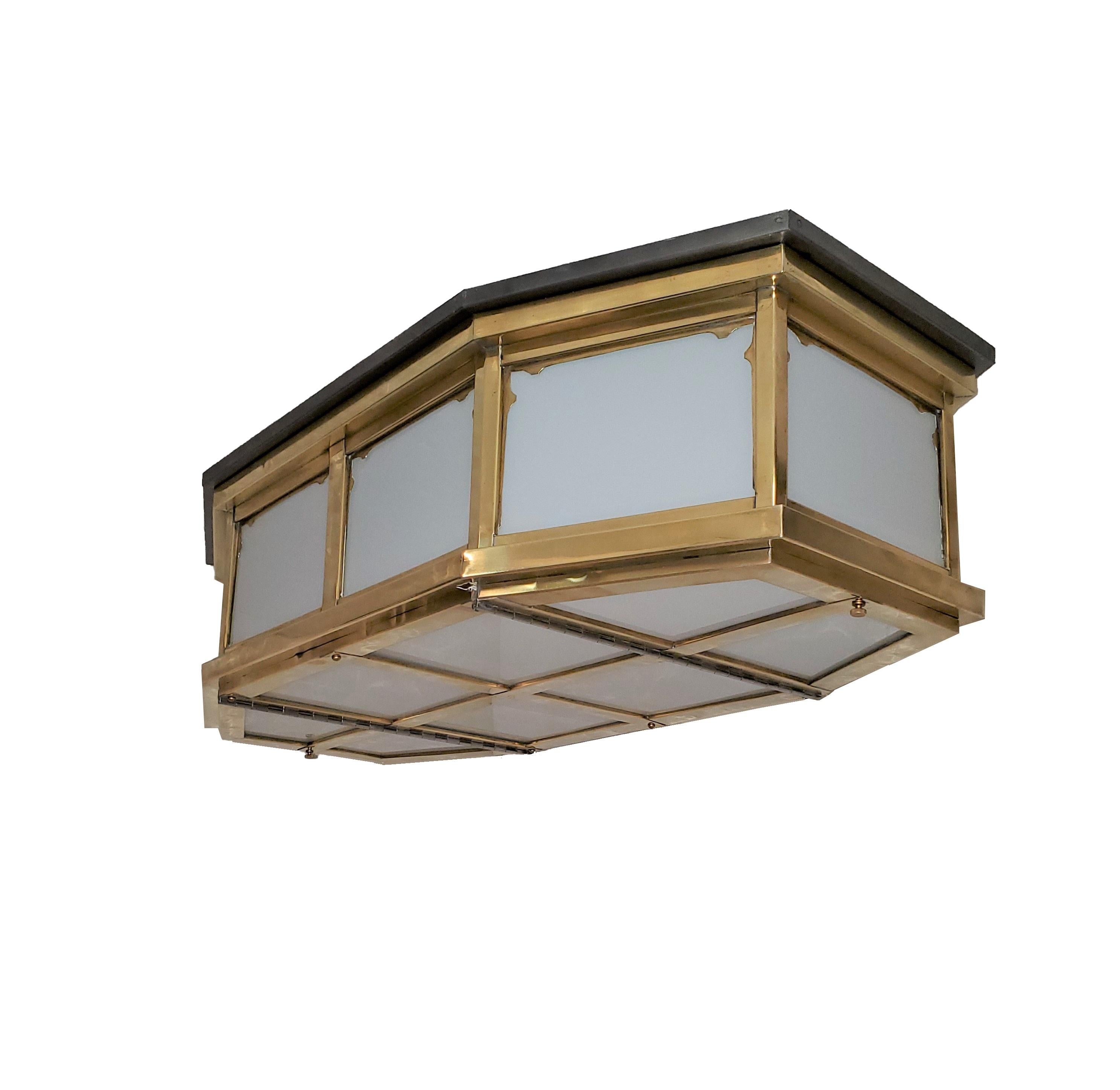A pair of Industrial, elongated octagonal flush mounted glass fixtures with brass stepped design frame. The eight sided shape features opaque white glass panel insets each circumvented by a decorative frame surround and ending with a grid like,