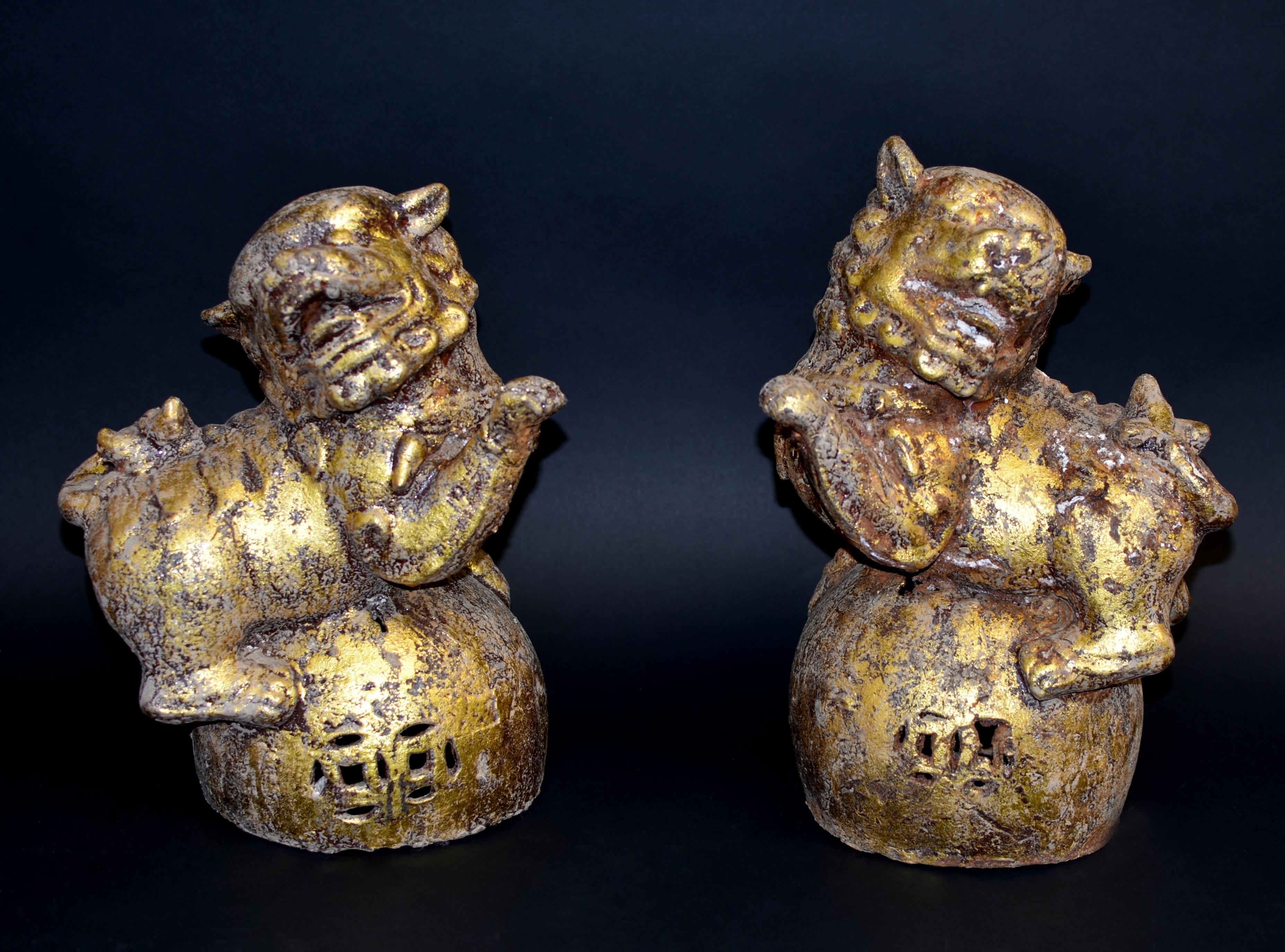 A pair of gilded iron foo dogs weighing a whopping 40 lb. Each well-fashioned in a perched position, the large head tilted with open jaws, large eyes and framed by a tightly curled mane. One of the paws raised and suspended in the air in a playful