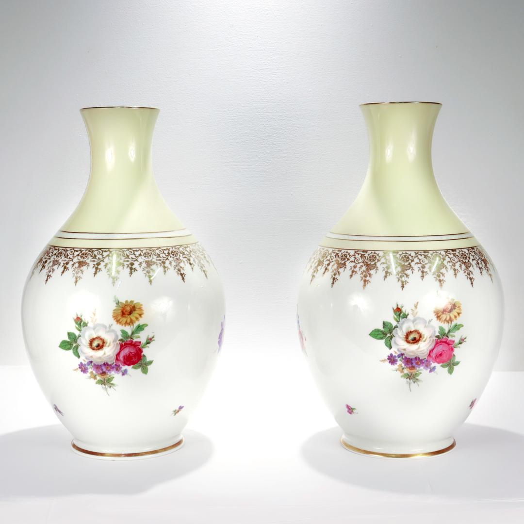A fine pair of large German porcelain vases.

By Rosenthal.

With a bulbous body and flaring neck.

Each with 4 floral sprays on a white ground with intricate gilt vine accents throughout. The neck is cream or ivory colored. Both the rim and the