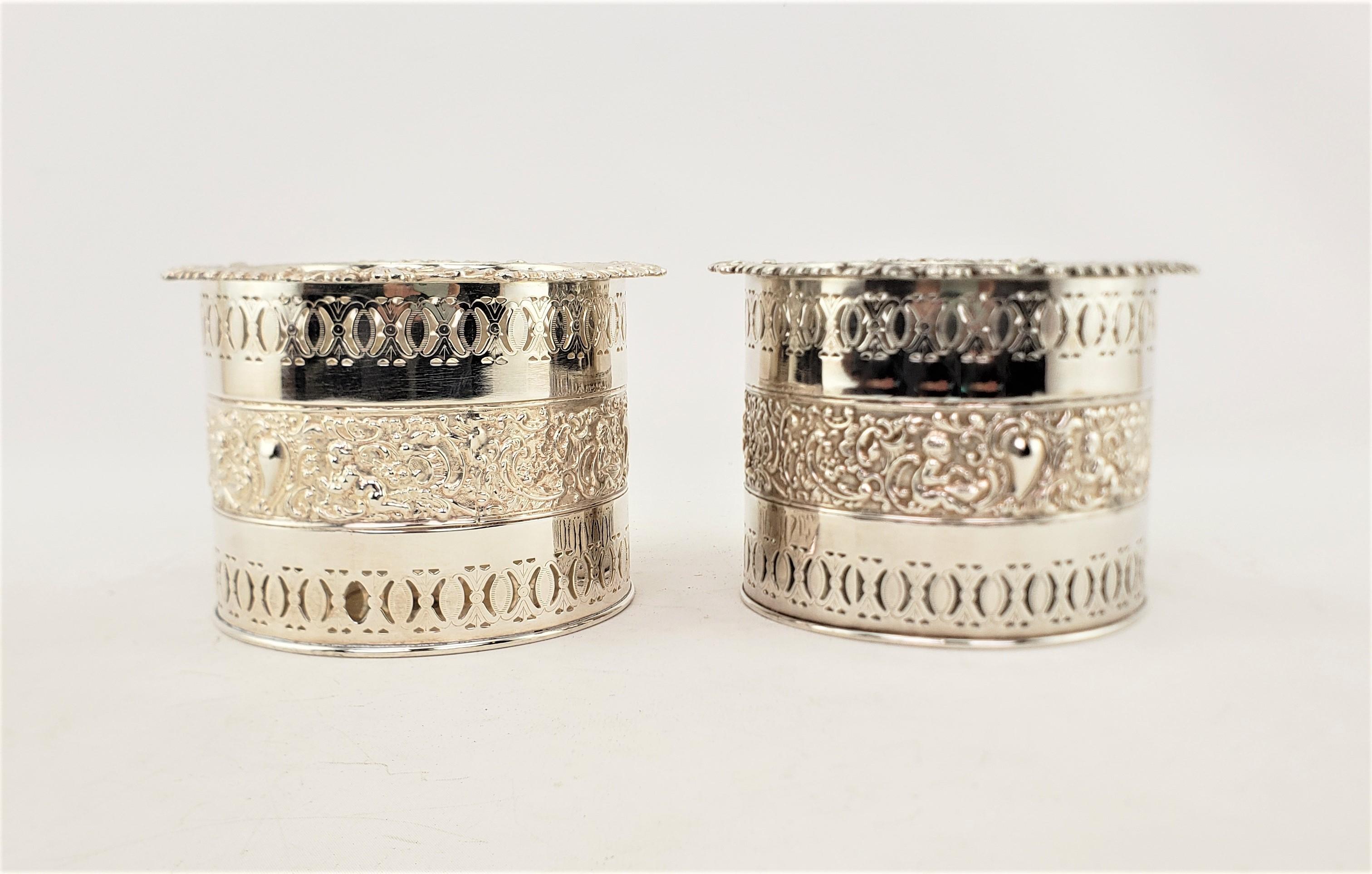 This pair of large bottle coasters are hallmarked by an unknown maker, and presumed to have originated from England and date to approximately 1920 and done in a Victorian style. The coasters are made of silver plate and have high pierced sides with