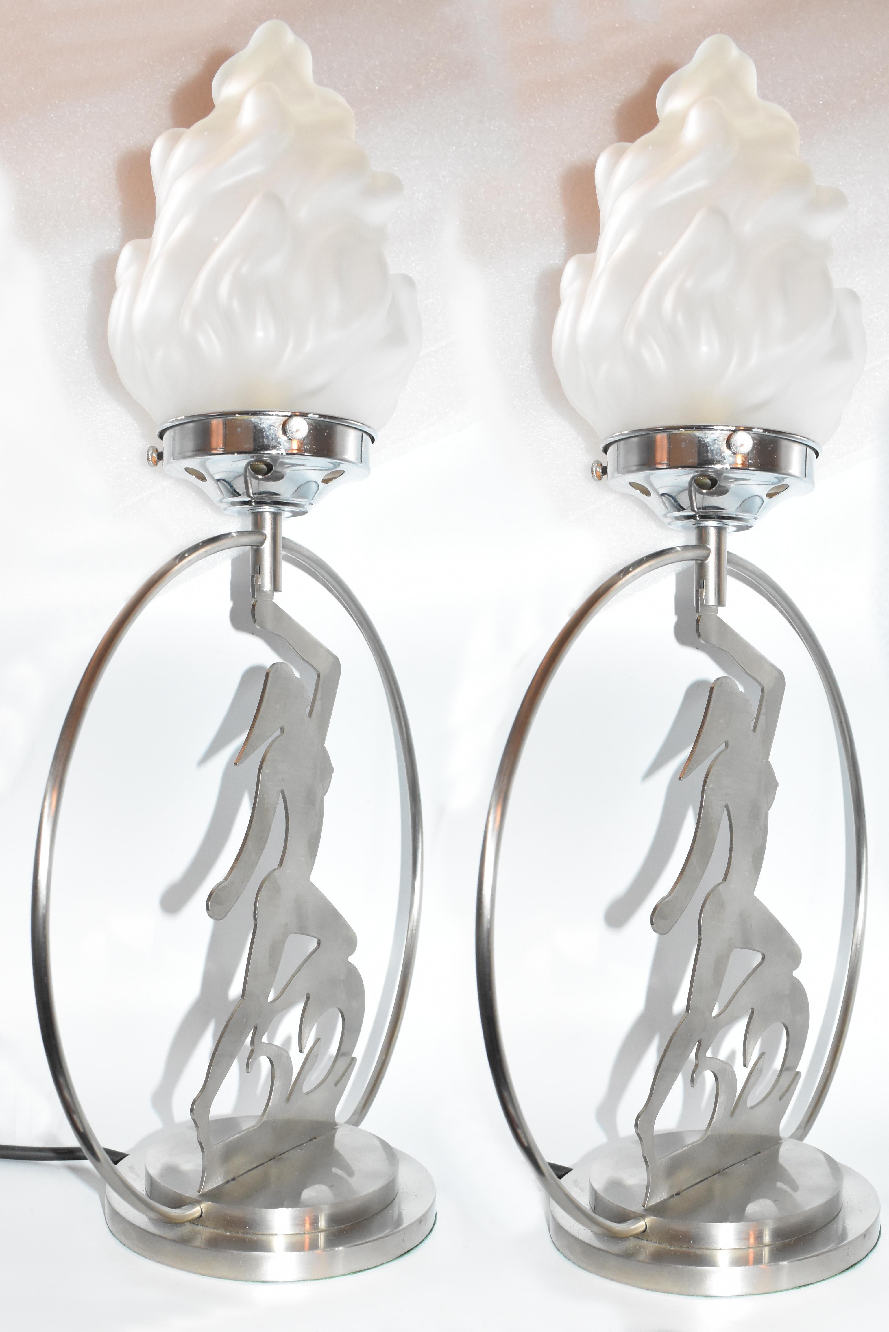 For your consideration are these Art Deco matching pair of table lamps. Both lamps depict a 2 dimensional female nude which supports a torch flame opaque glass shade. The body of the lamp seems to be a dulled chrome as opposed to the gallery which