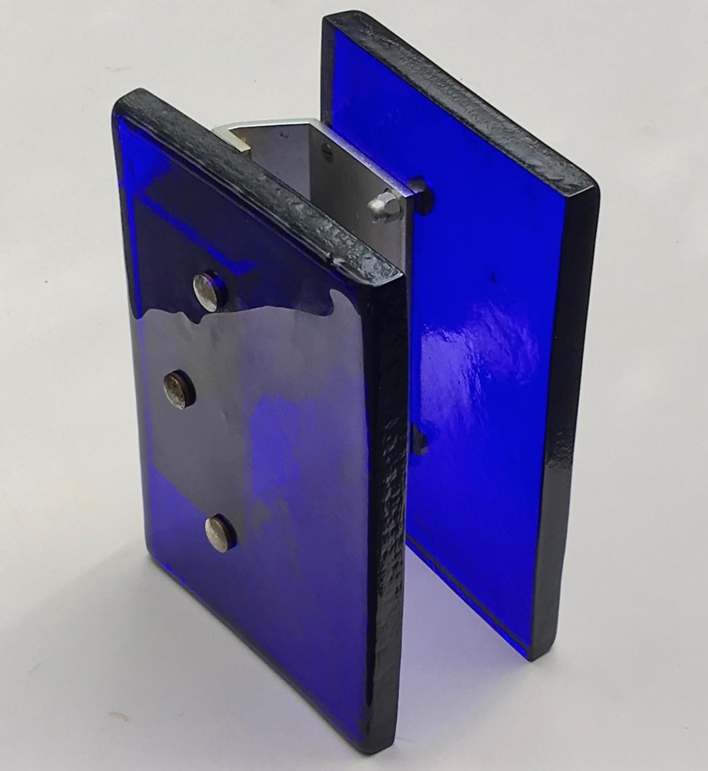 A pair of large glass push-pull door handles of simple rectangular form, with aluminium brackets.

These are heavy pieces, made of thick hand-formed glass in deep blue. The glass attaches to the aluminium brackets using three bolts; from the finish