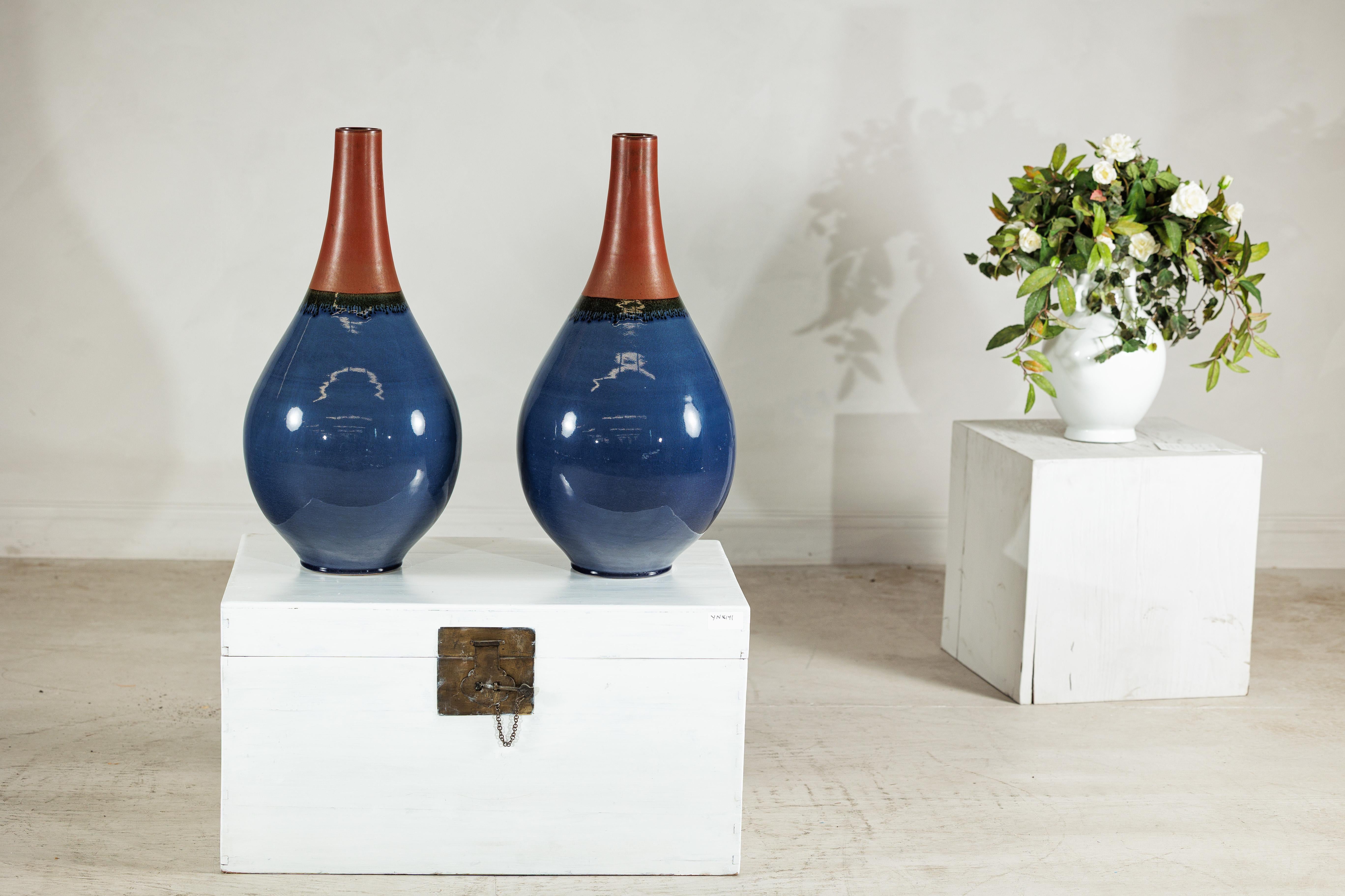 A commanding pair of large-scale artisan ceramic vases, distinguished by their graceful teardrop silhouette and richly layered glazes. Each piece transitions from a deep, lustrous blue body to a matte terracotta neck, the two tones meeting in a